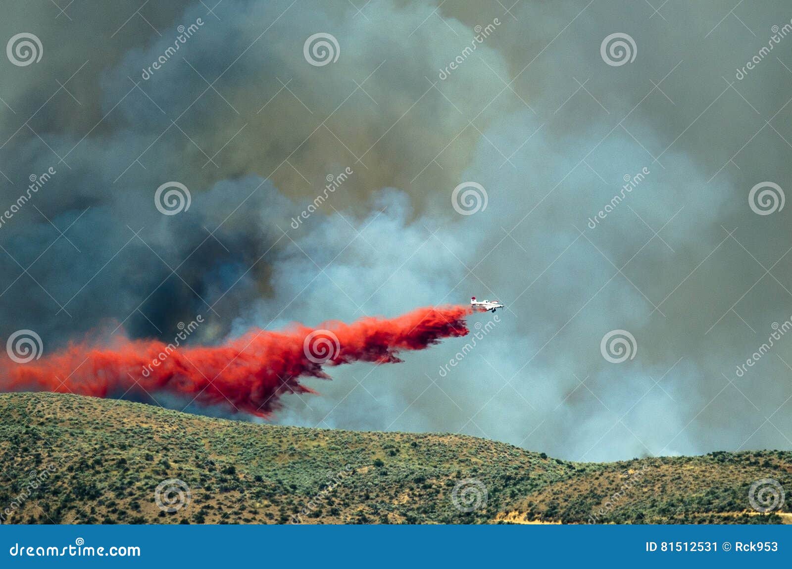 white aircraft dropping fire retardant as it battles the raging wildfire