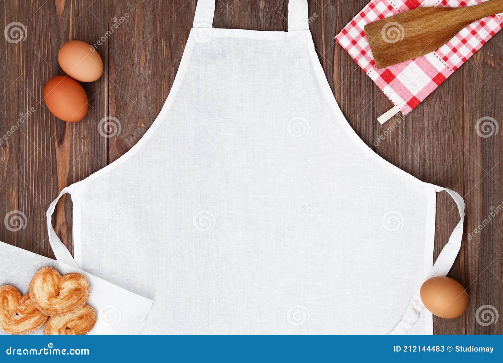 blank white apron template on wooden table with cookies and eggs, copy space. kitchen, cooking clothing mockup