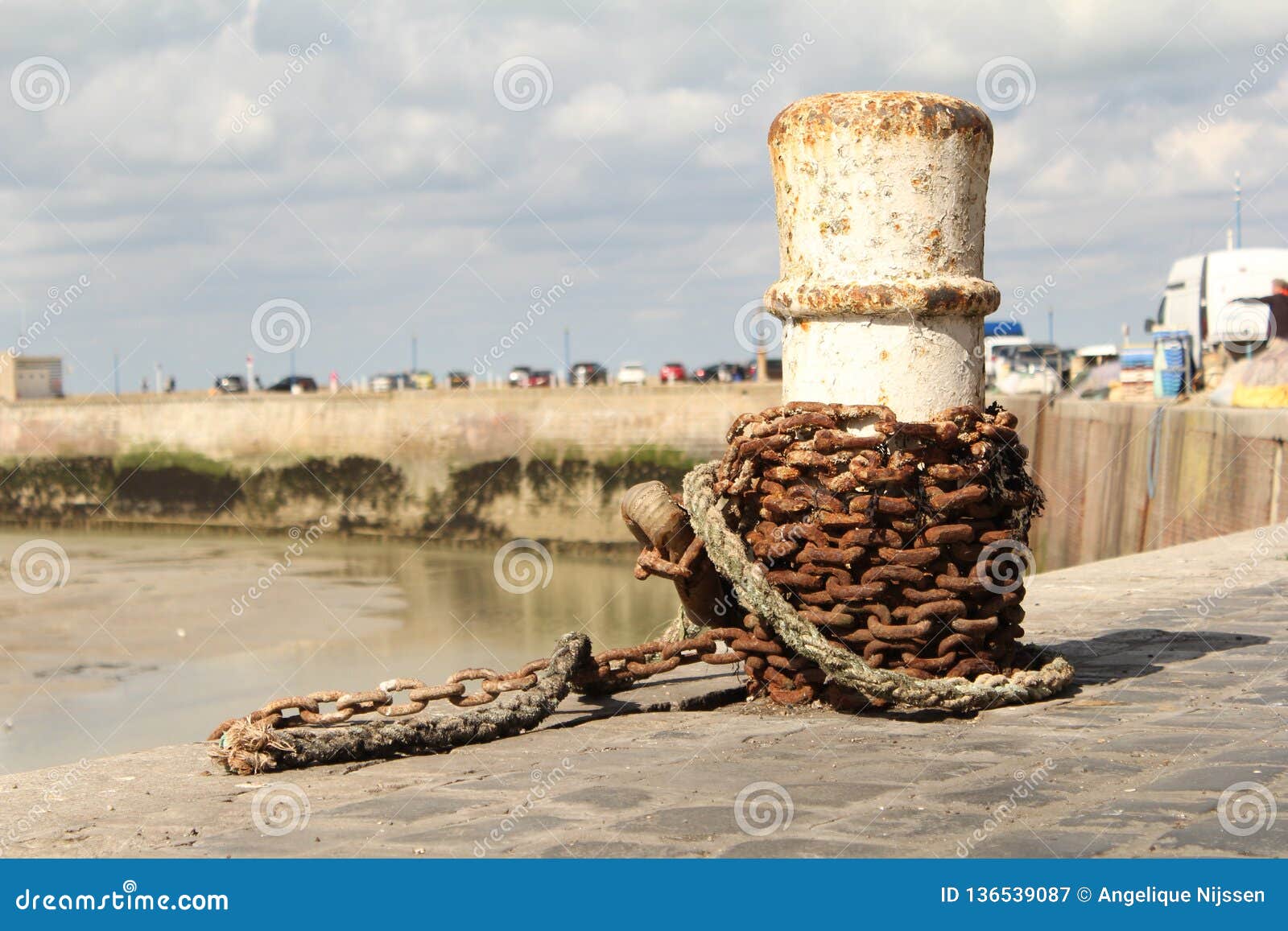 A white bollard with a rusty chain closeup at the harbour in normandy. A white bollard with a rusty chain macro at the quay in the harbour in saint-valery-en-caux, normandy, france in summer