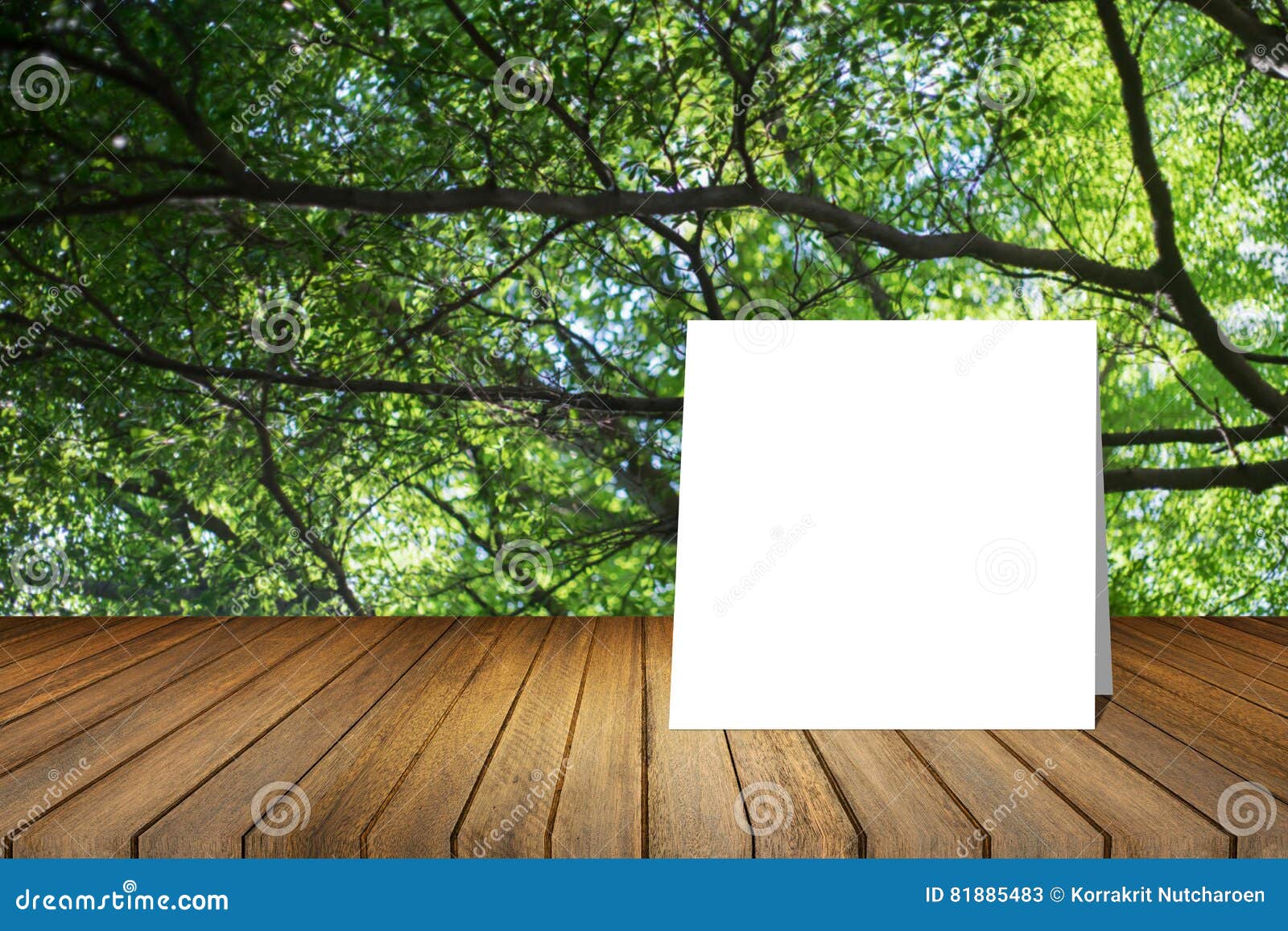 white card put on wooden desk or wooden floor on blurred green tree nature background.use for present or mock up your product.