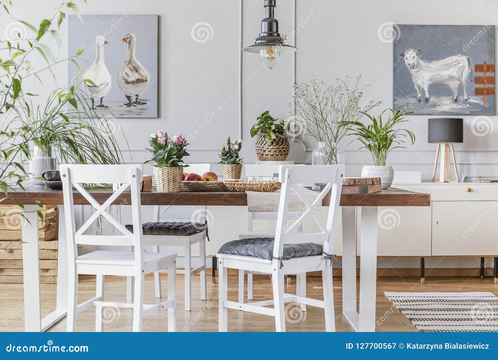 white chairs at wooden table with flowers in eclectic dining room interior with posters. real photo