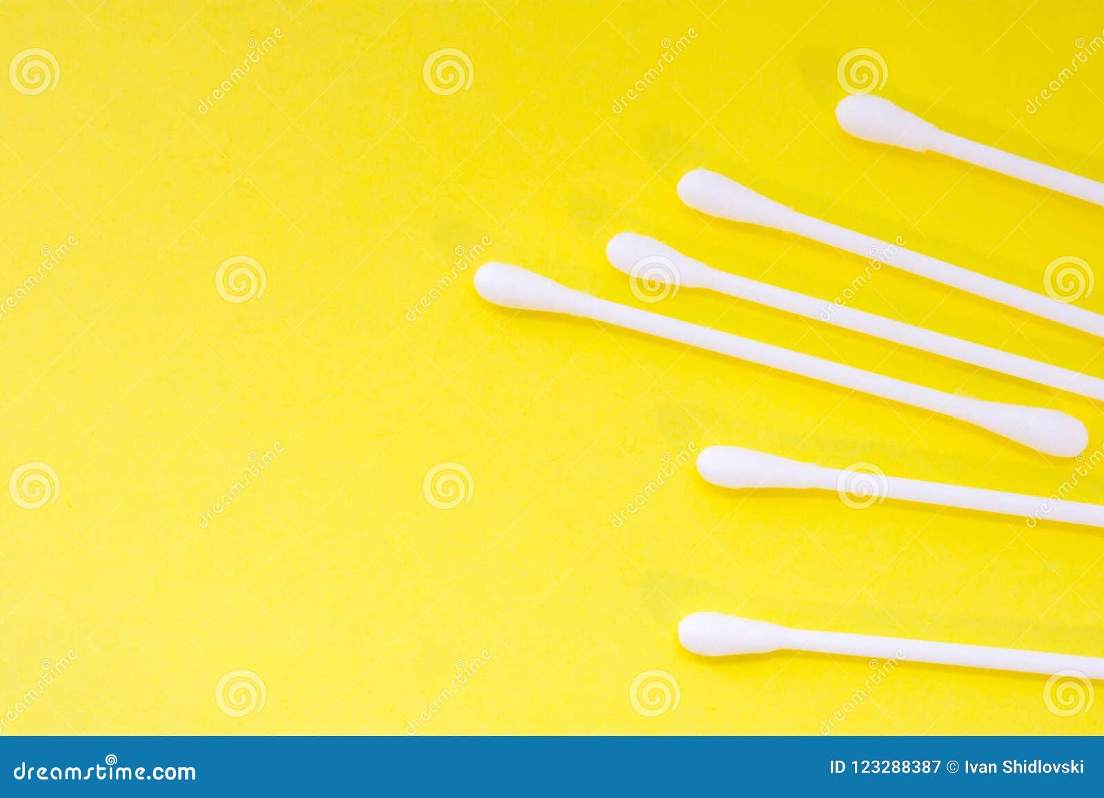 white cotton swabs or buds are on yellow uniform background view from above with clear area of half of photo for labels or headers