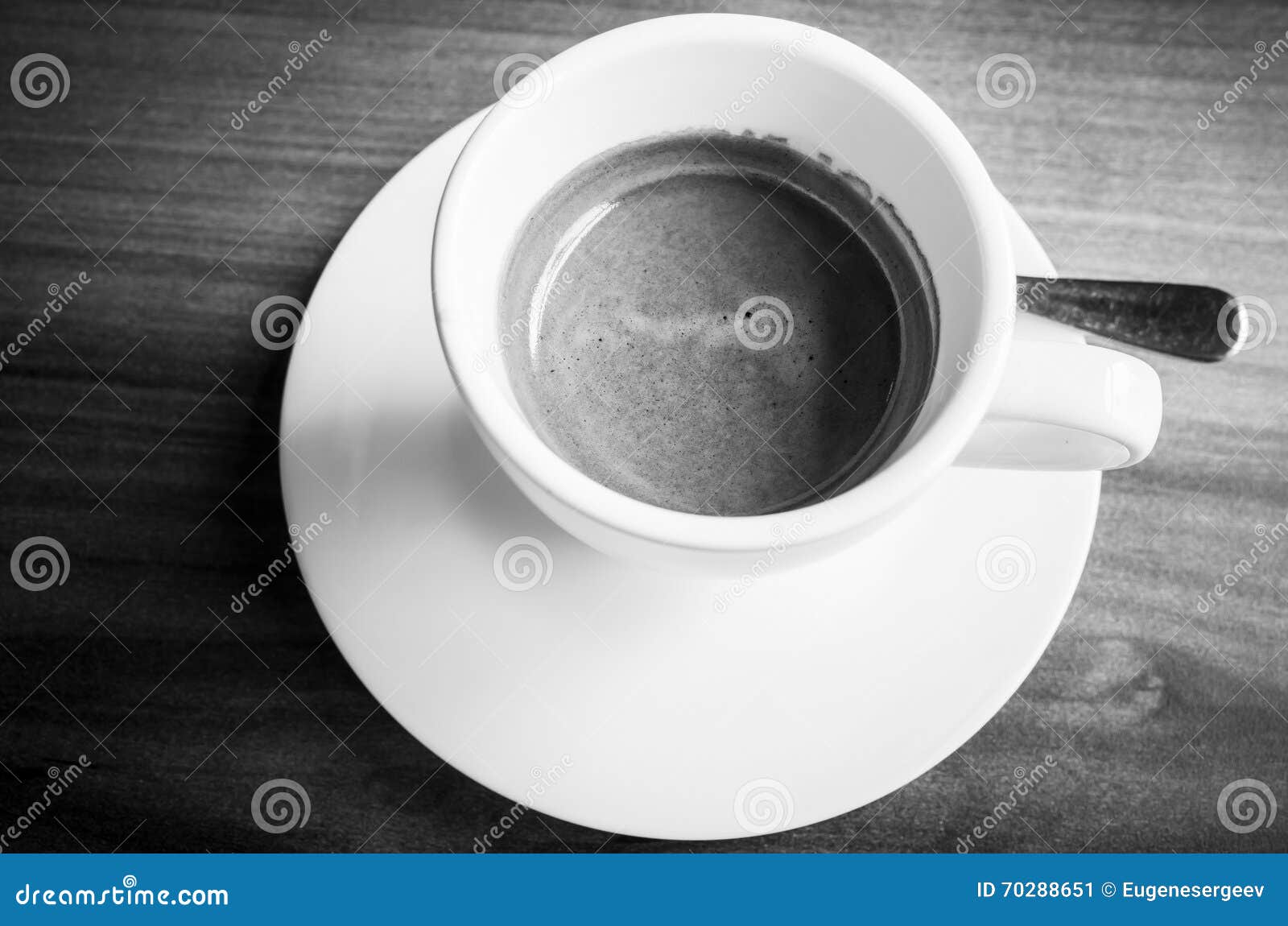 White cup of freshly brewed espresso coffee on saucer with spoon. Black and white photo with selective focus