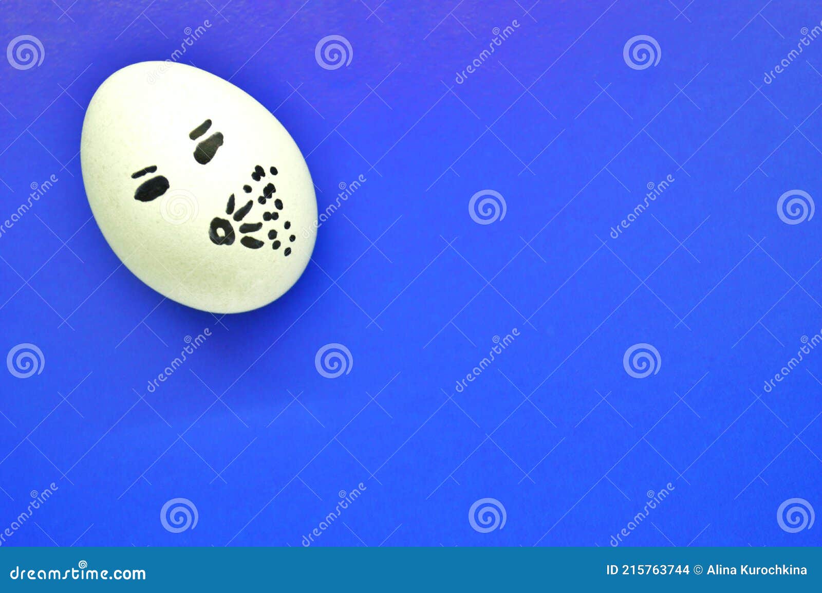 White Egg with a Painted Sneezing Face on Blue Background Stock Photo