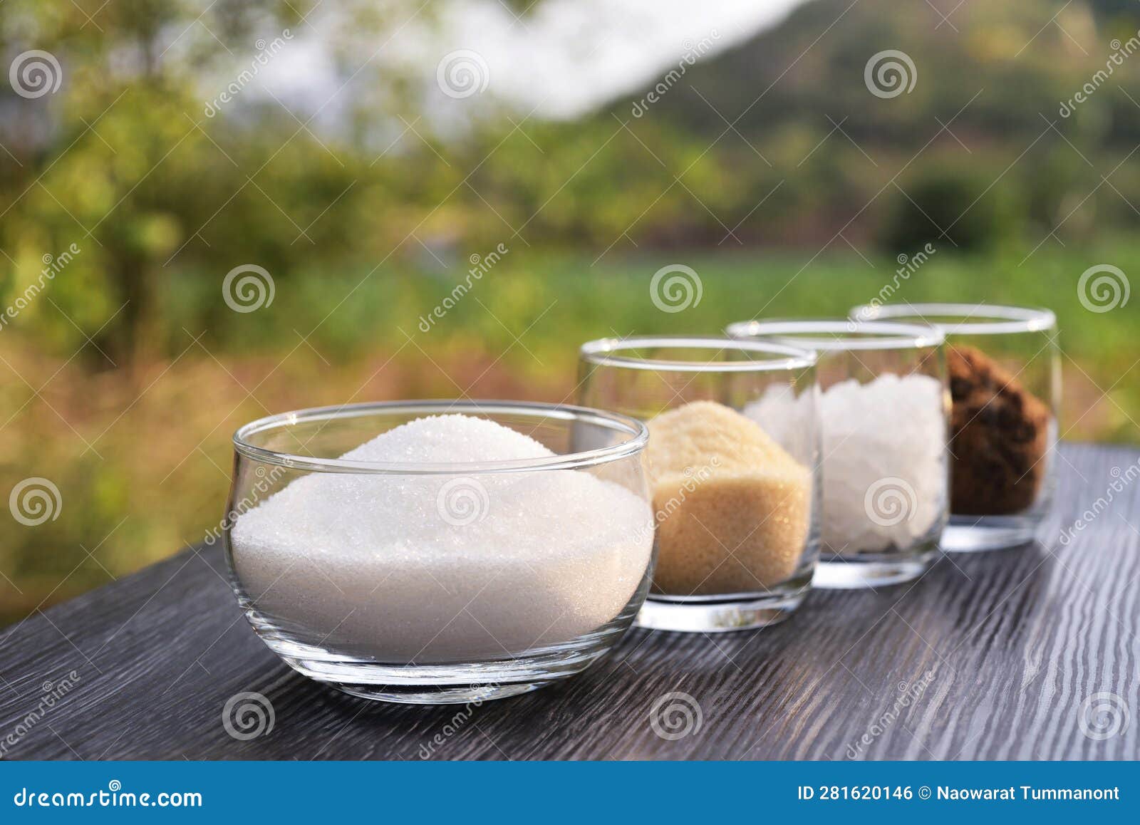 white granulation sugar, raw sugar , crystalline sugar and brown sugar in line of clear glasses with natural mountain view backgro