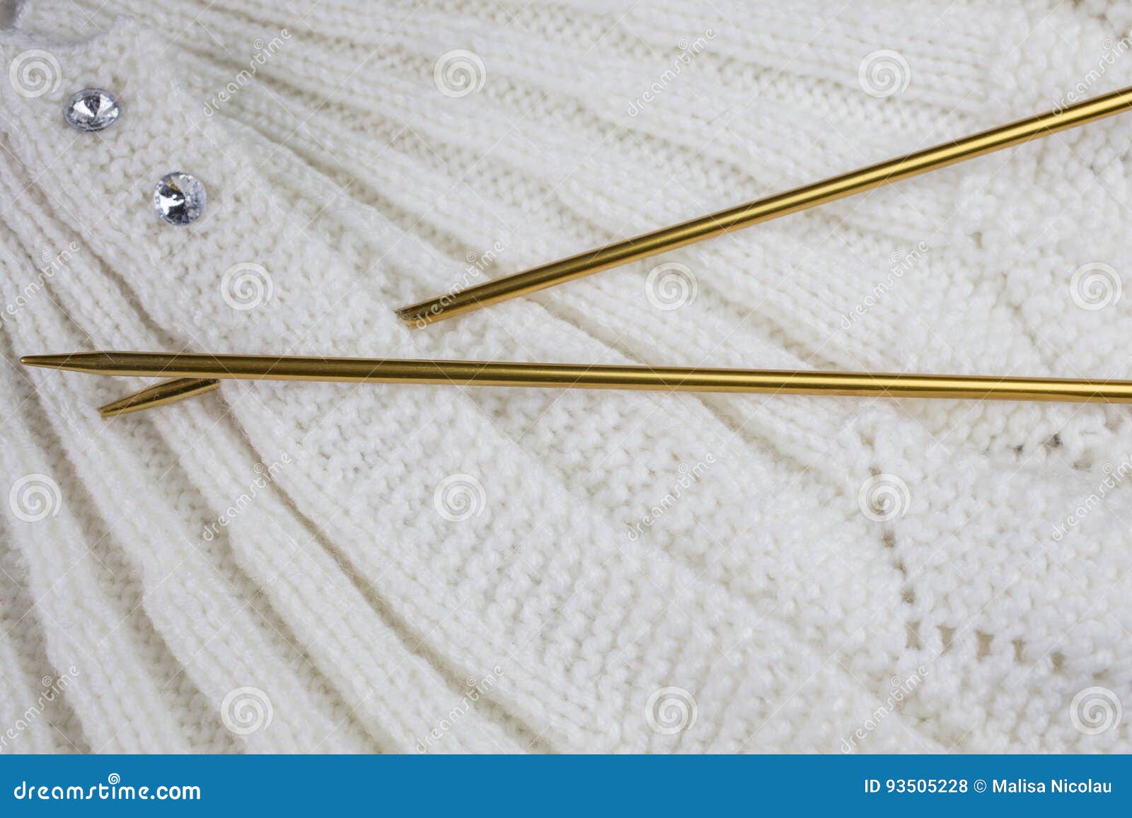 White Knitted Garment with Gold Colored Knitting Needles Stock Photo