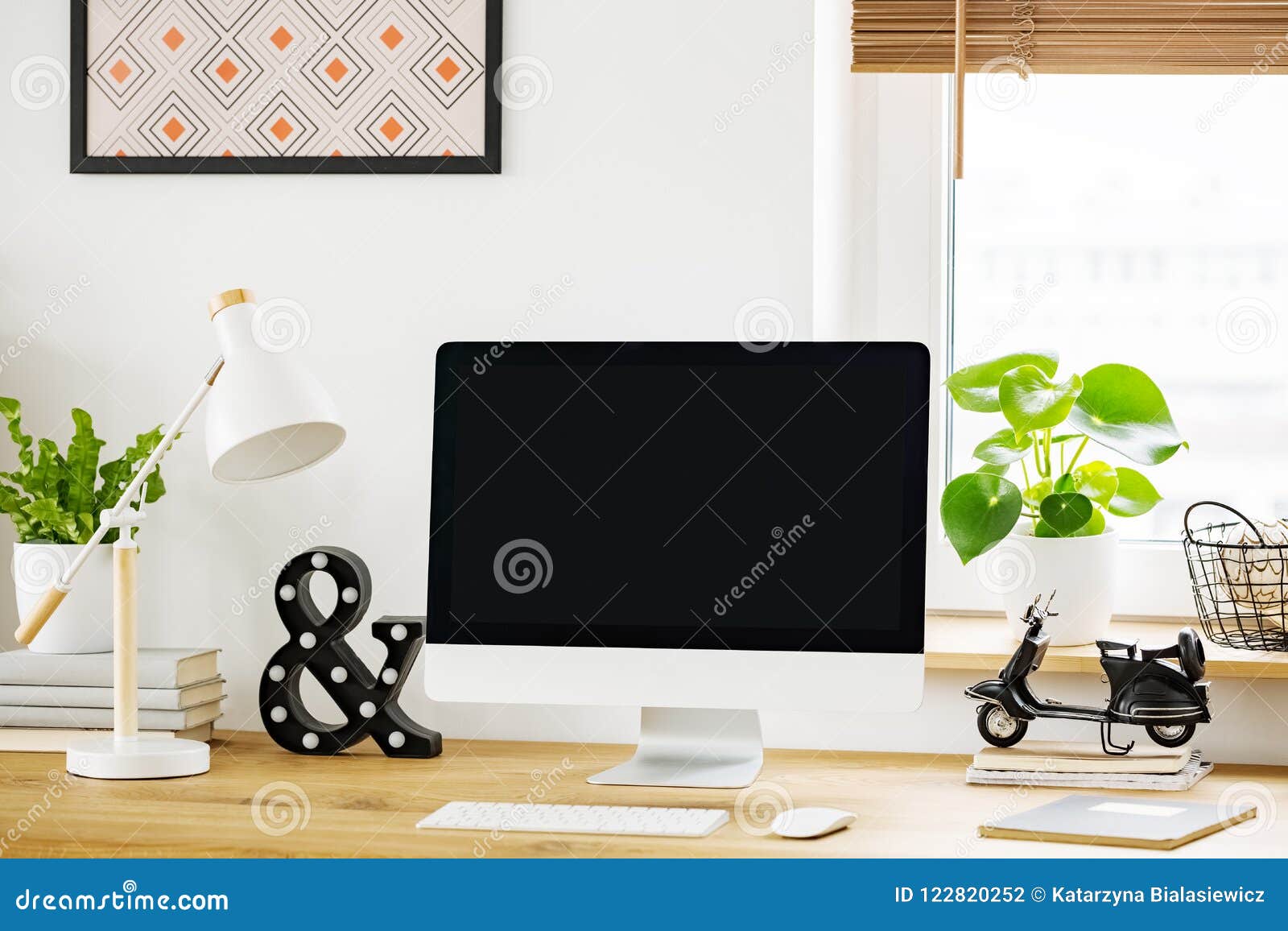 white lamp next to computer desktop on wooden desk in home office interior with plant. real photo