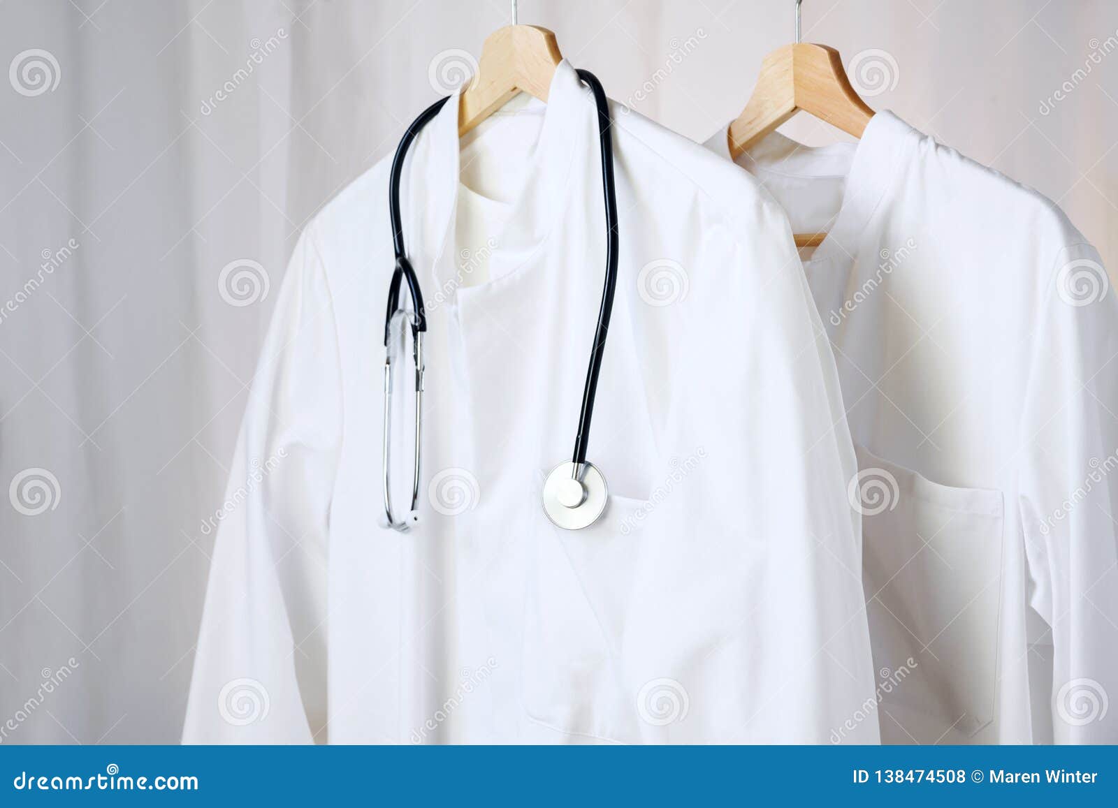 white medical doctor or physician lab coats with stethoscope hanging on clothes hangers, copy space