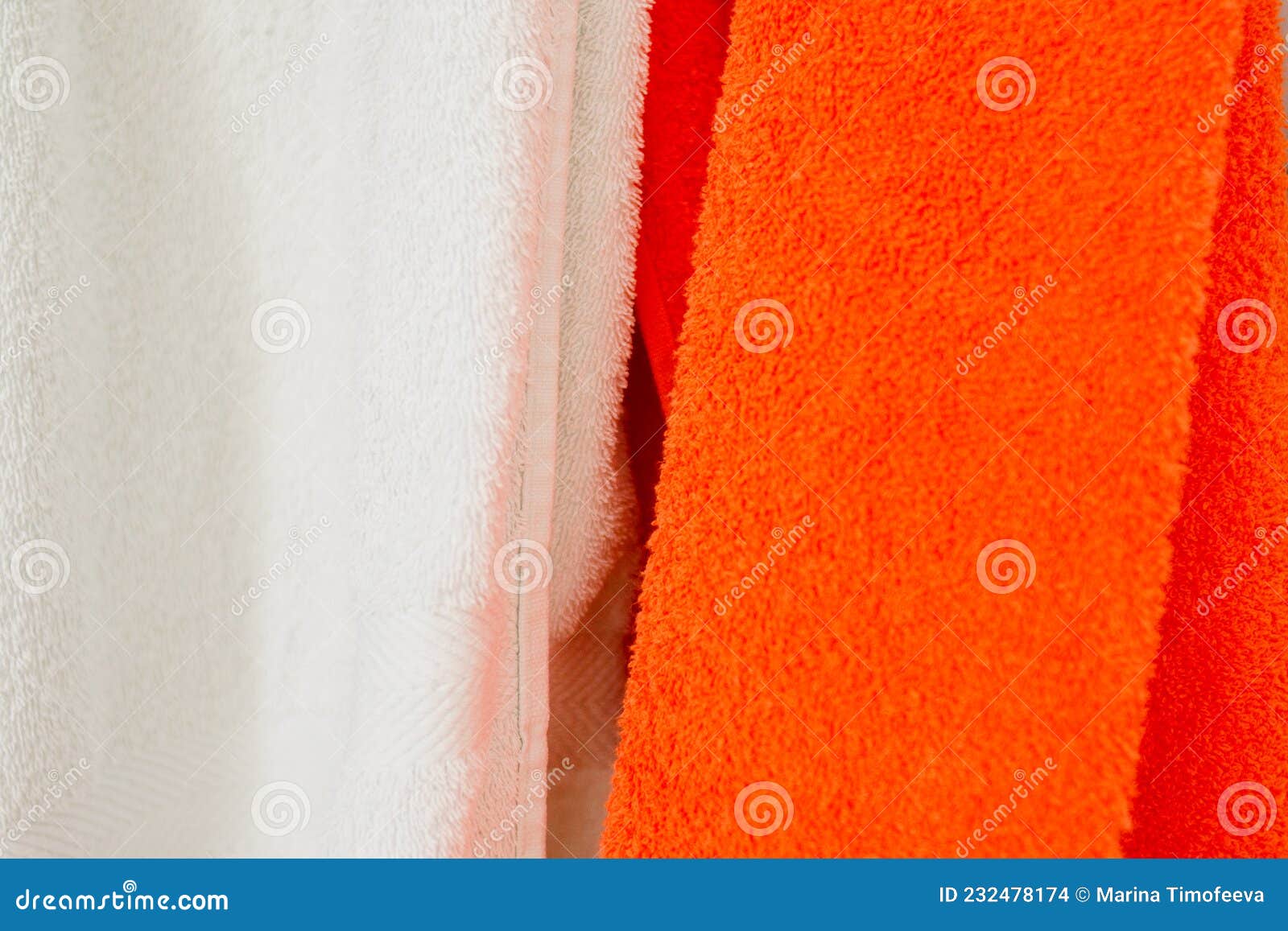 White and orange towels hang side by side. Horizontal photo of fabric texture close-up