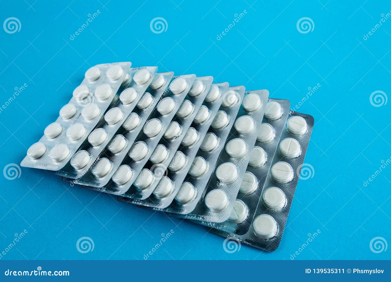 White Round Pills in Pack. Tablets are Next To the Packaging on a Blue