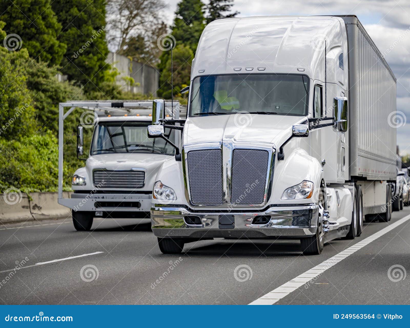 white small and big rigs semi trucks with semi trailers running side by side on the wide multiline highway road
