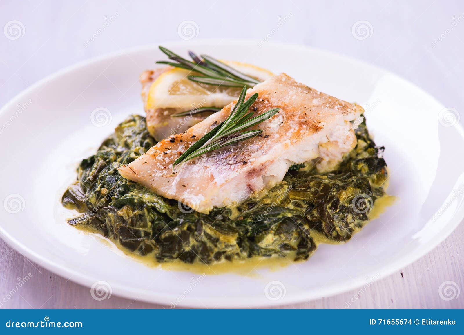 White Stewed Fish Fillet with Herbs on Fried Spinach Stock Photo