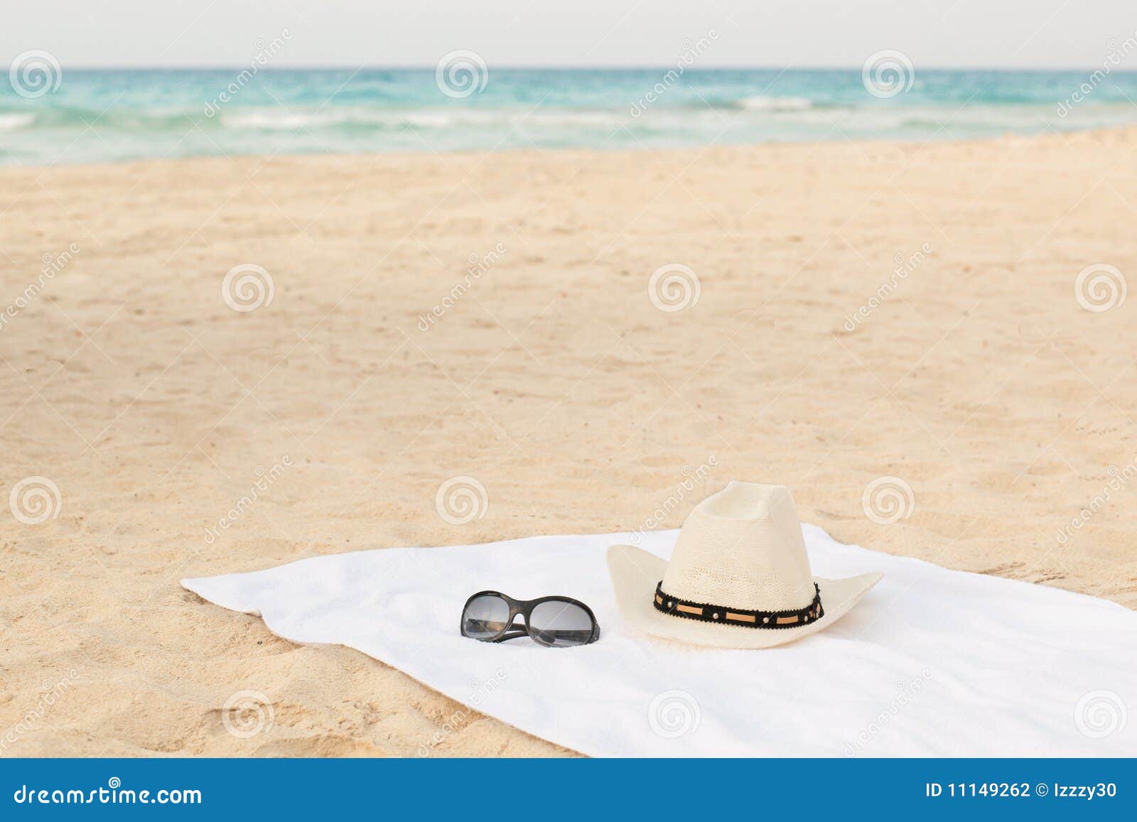 white towel on the beach with sunglasses and hat