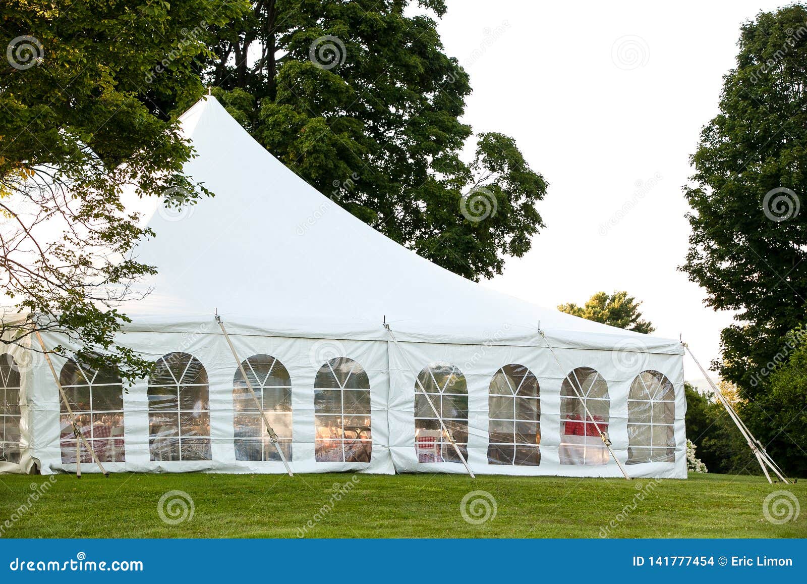 a white wedding tent set up in a lawn surrounded by trees and with the sides down