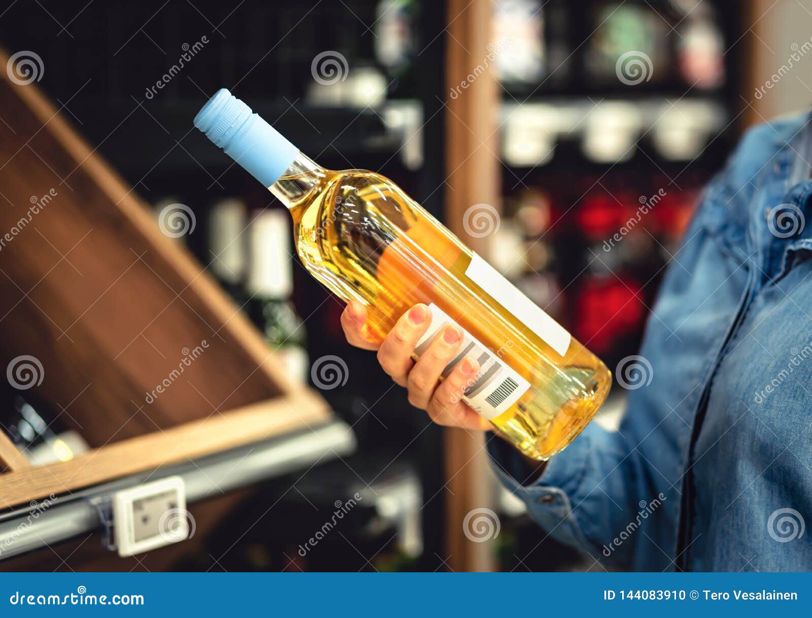 white wine bottle in hand in liquor store. customer buying alcohol. woman choosing the right bottle of chardonnay or riesling.