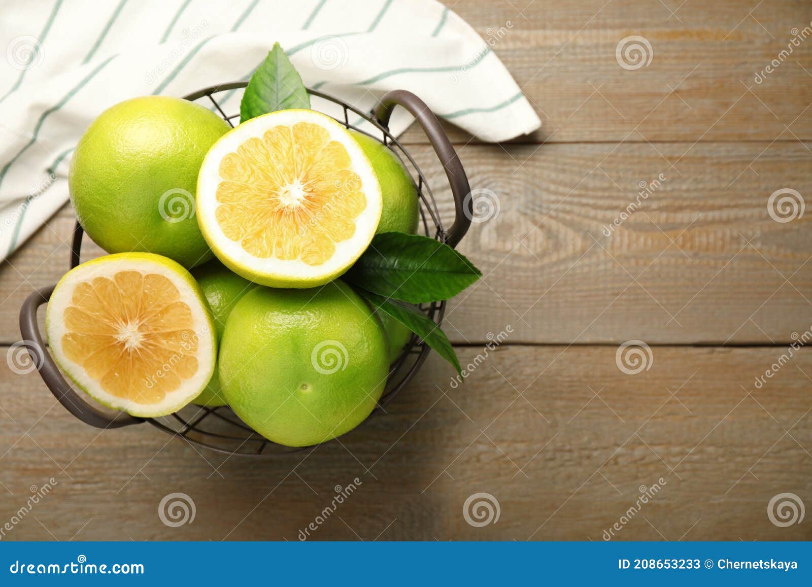 whole and cut sweetie fruits in metal basket on wooden table, flat lay. space for text