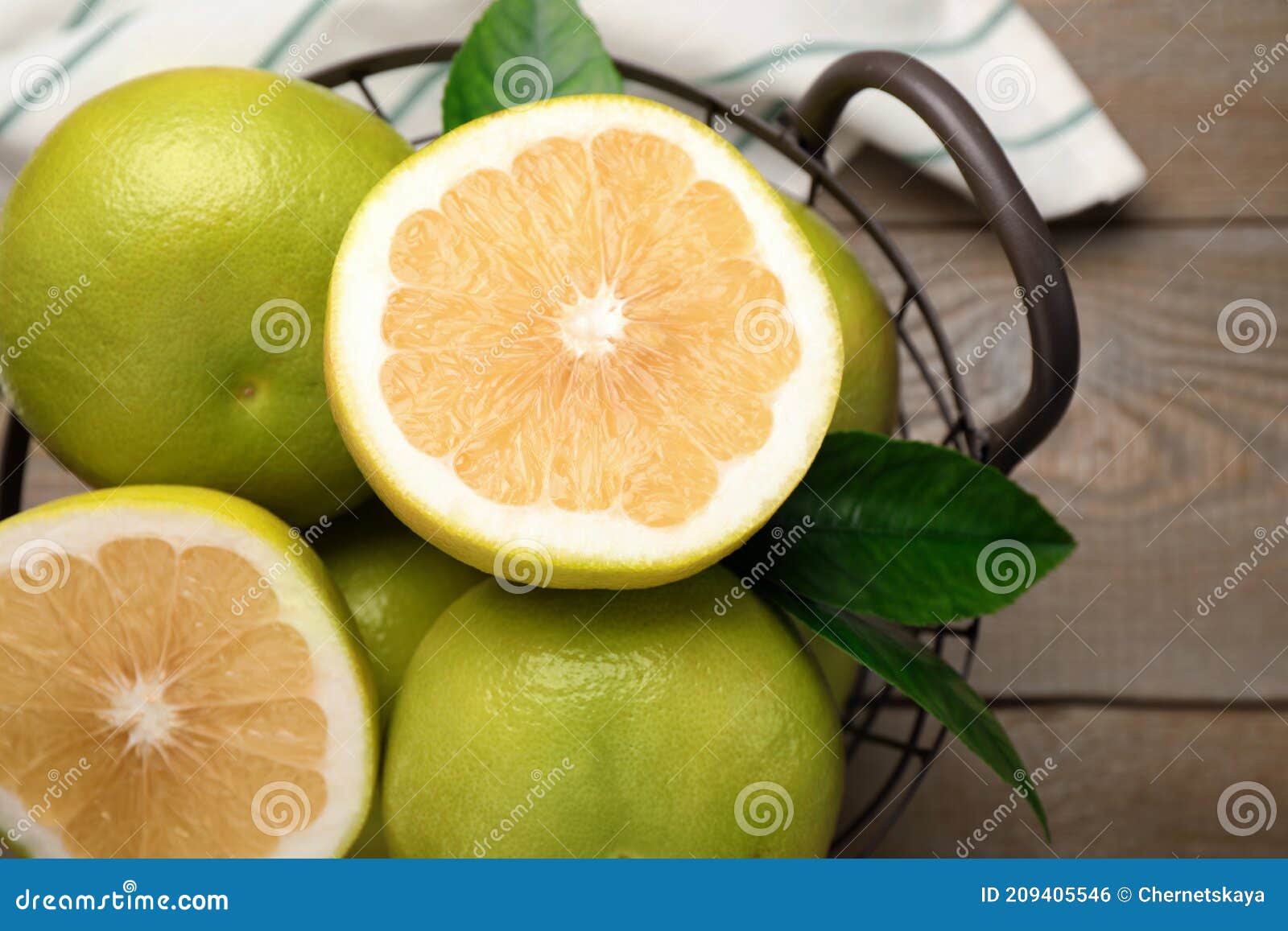 whole and cut sweetie fruits in metal basket on wooden table, top view