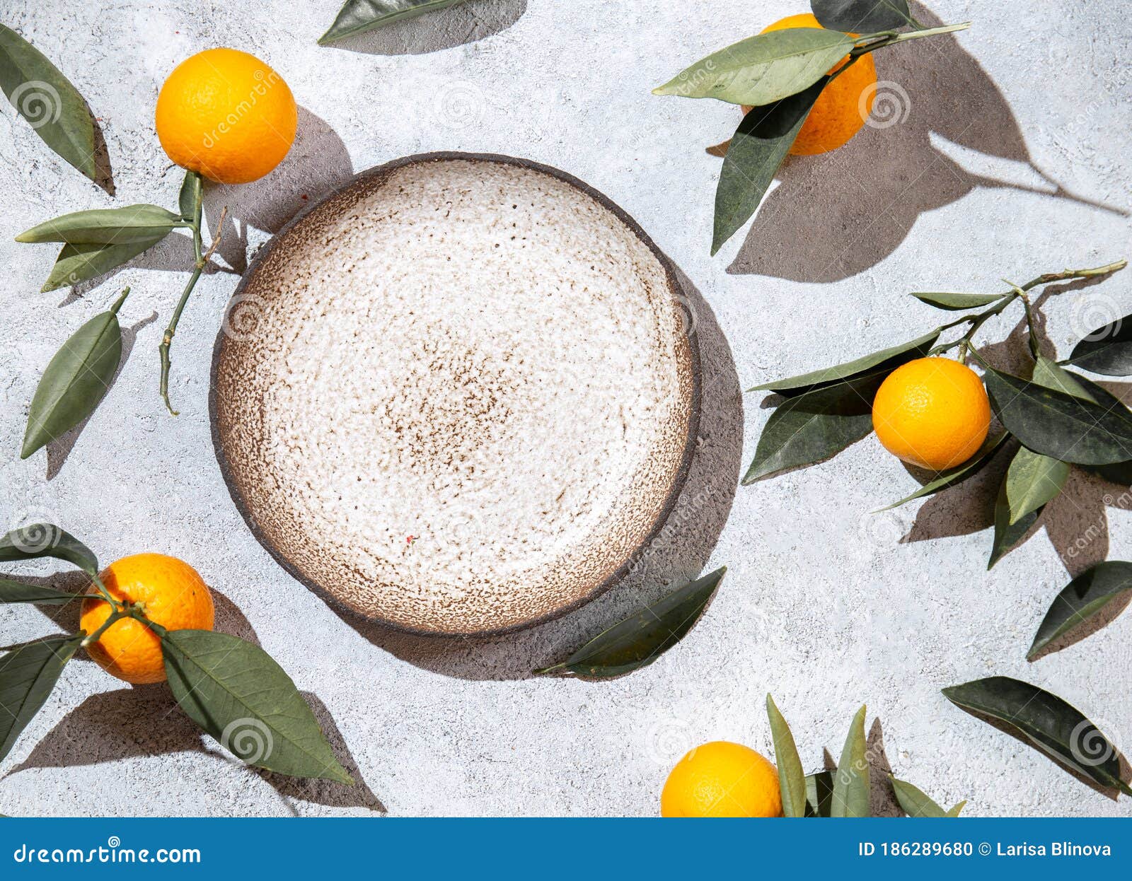 whole oranges witl orange tree leaves on white background around empty plate. top view, flat lay, summer and healthy