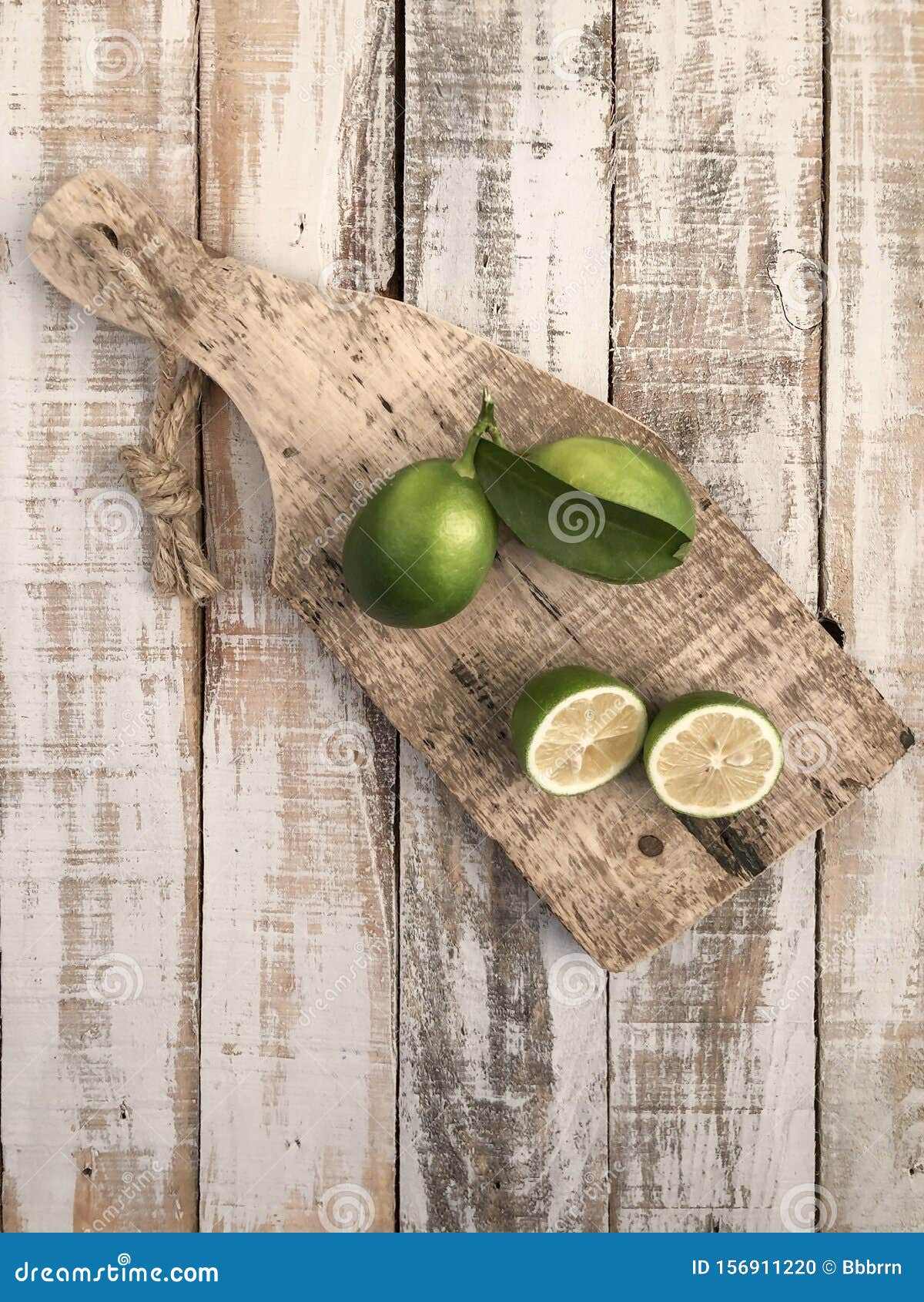 Whole and Sliced Limes on a Wooden Cutting Board on Table Stock Photo