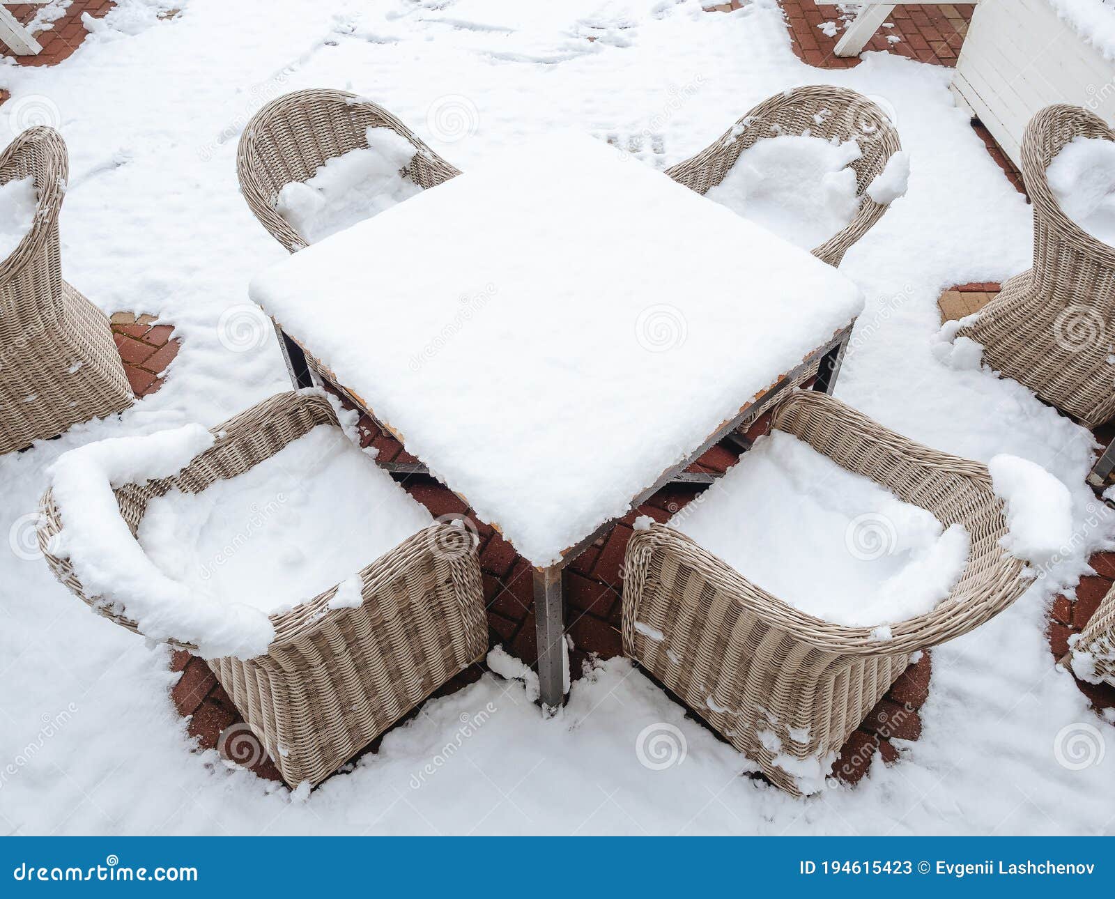 Wicker Chairs Strewn with Snow Stand Around a Snowstrewn Table on a
