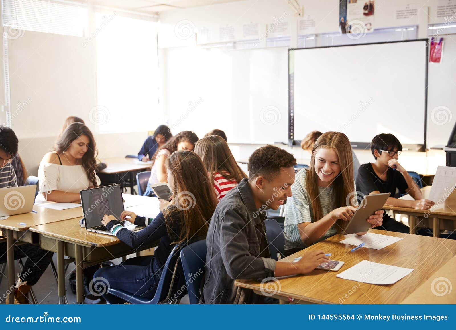 wide angle view of high school students sitting at desks in classroom using laptops