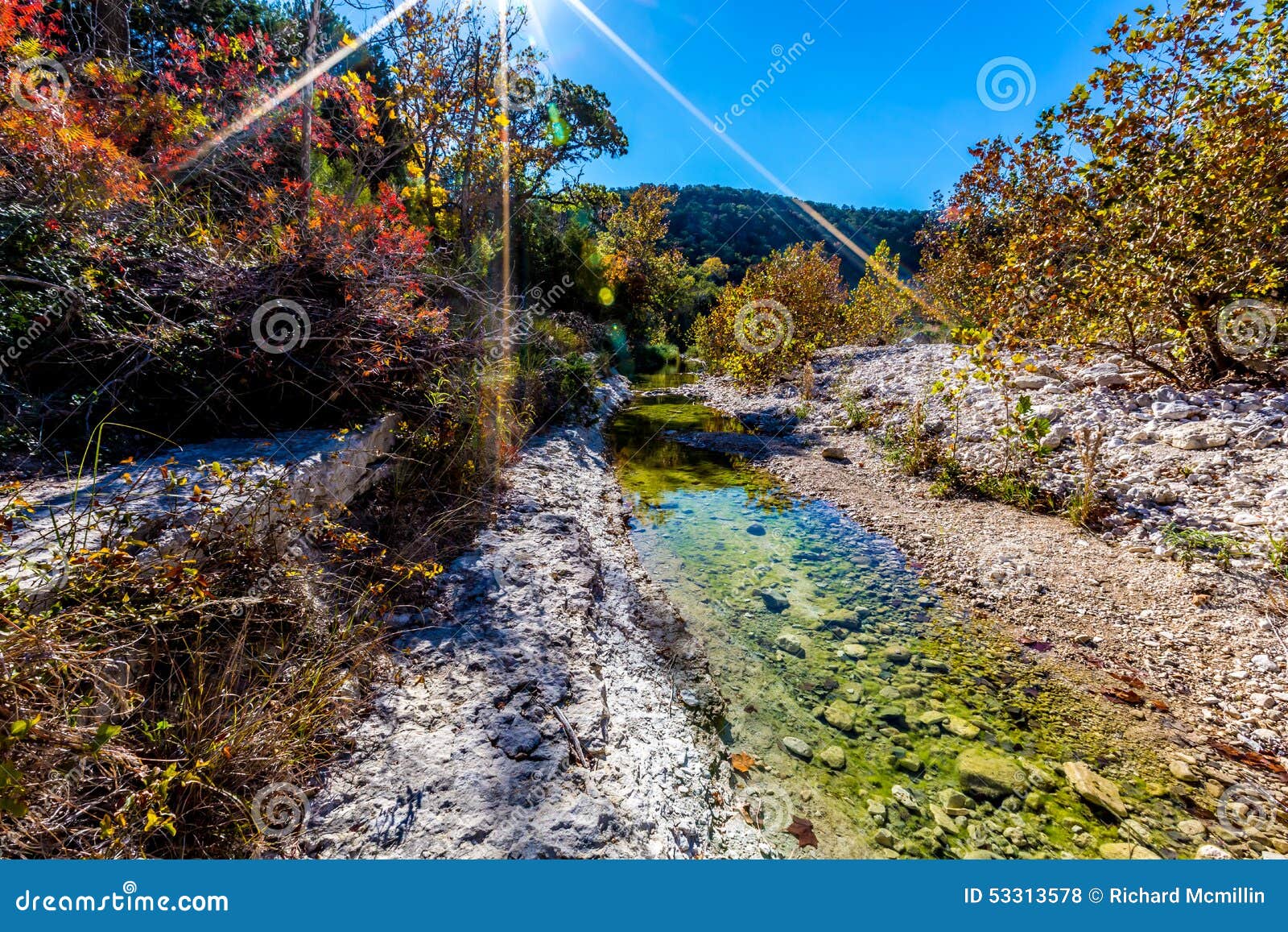 wide shot of a rocky stream surrounded by fall foliage with blue skies at lost maples