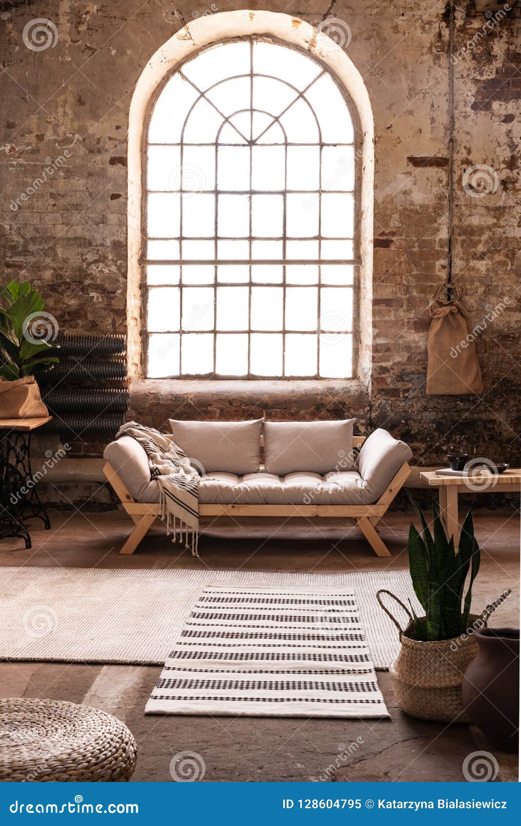 window above grey wooden sofa in spacious loft interior in wabi sabi style with plant and carpet