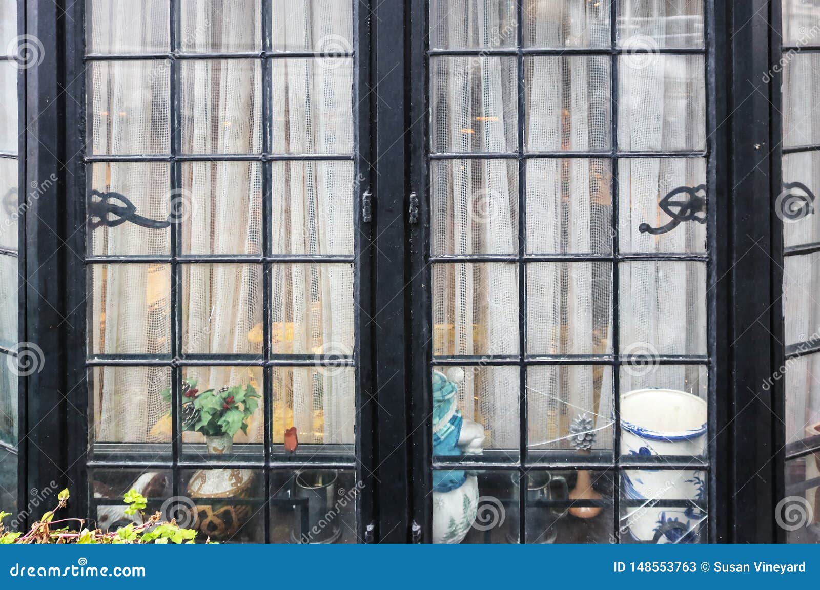 window of modest homey home - broken black metal bay window with net curtains and knick-knacks sitting inside