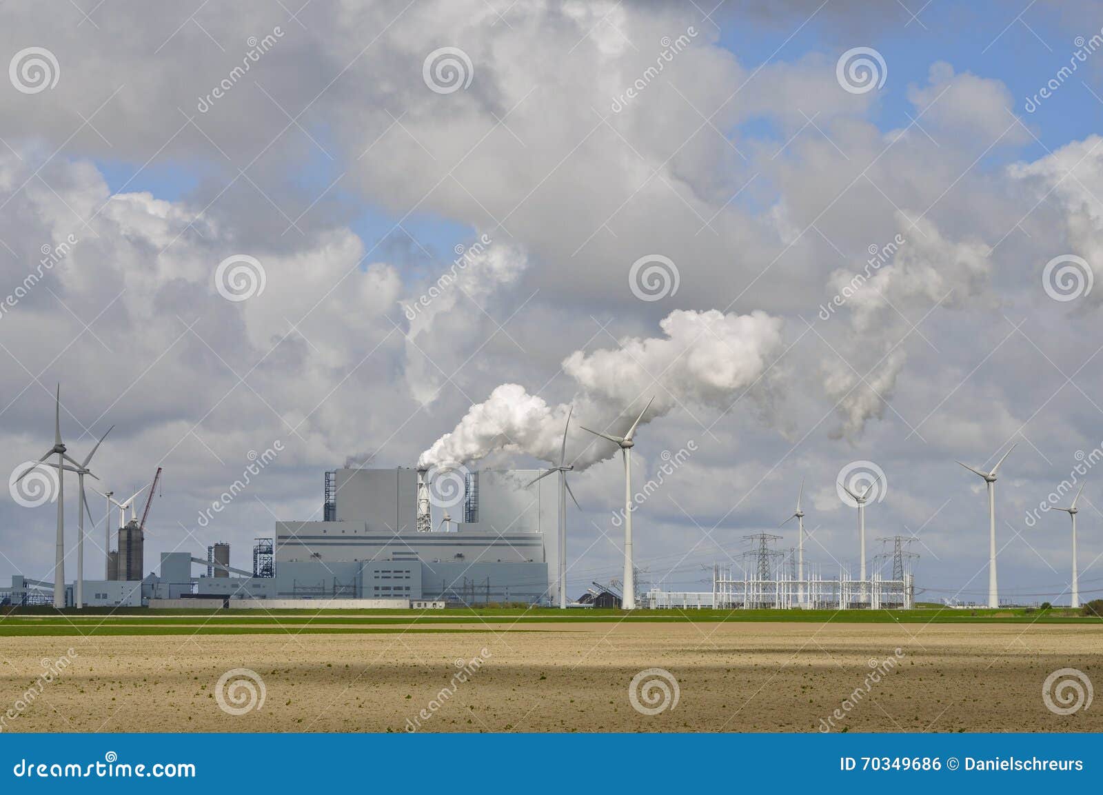wind powered generators line a large fossil fuel power plant