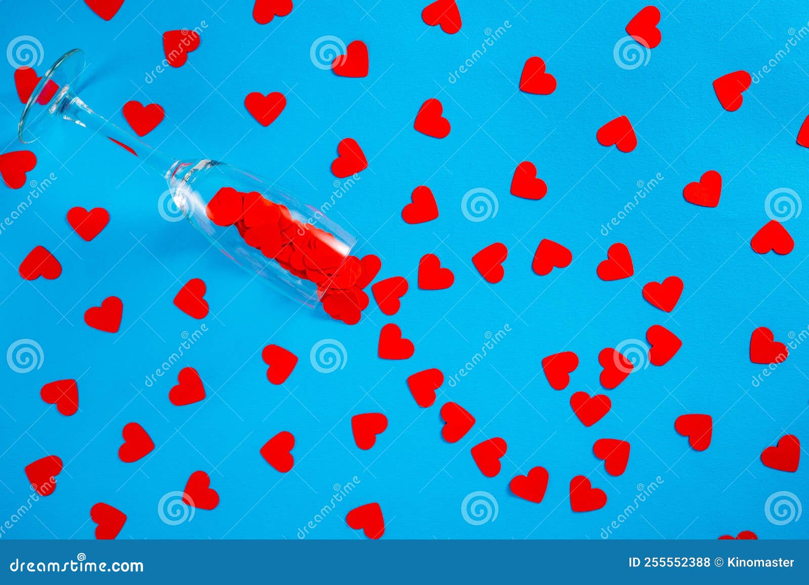 wineglass and pattern of paper red hearts on blue screen background. top view of heart d confetti arranged in a