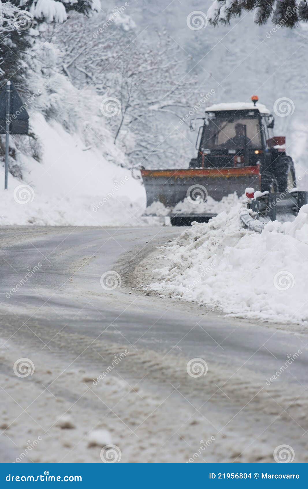 Winter time road with a snowplow. Tractor removing snow from a road while snowing