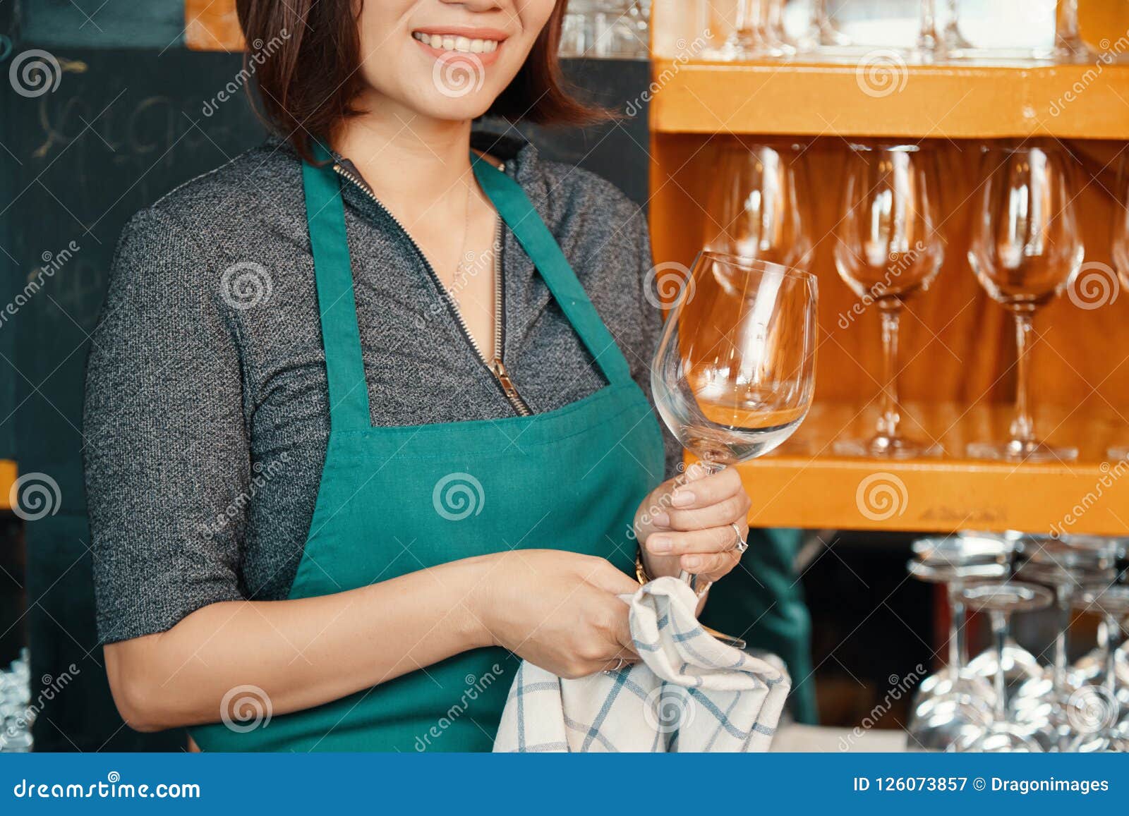 Smiling female bartender wiping glass with towel. Woman barista at