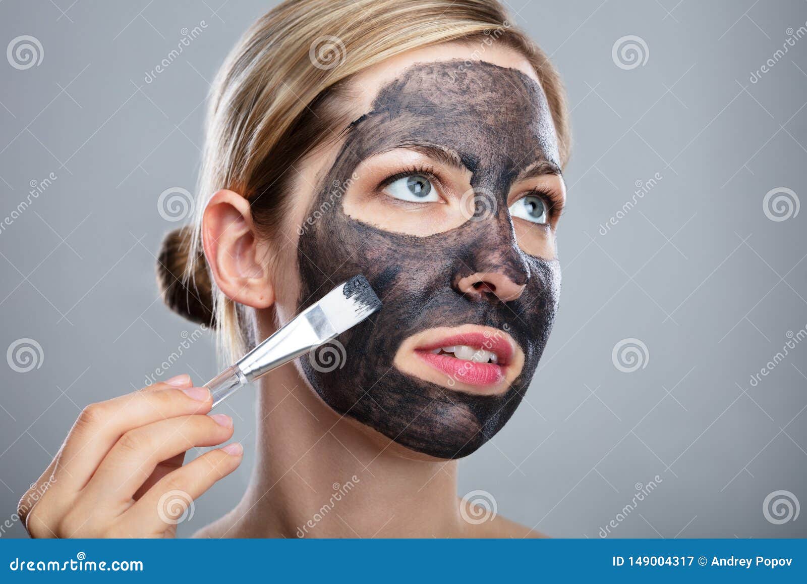 woman applying activated charcoal face mask with brush