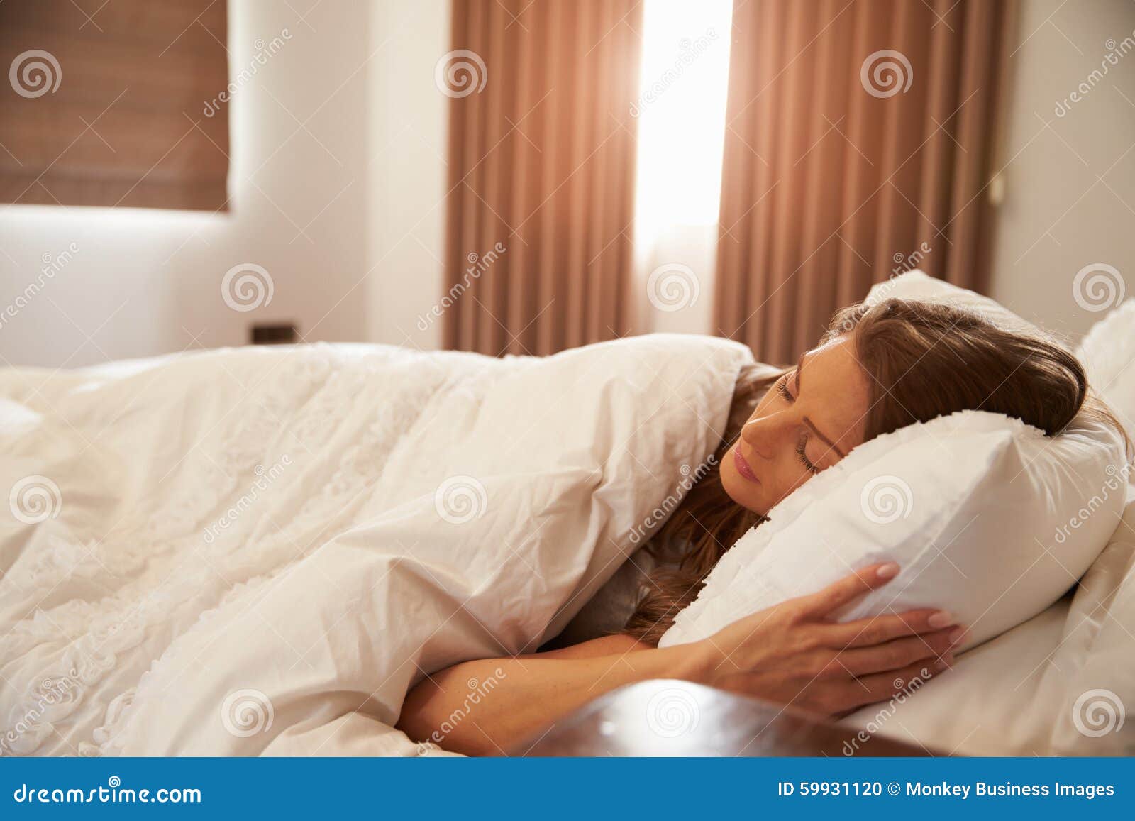 woman asleep in bed as sunlight comes through curtains