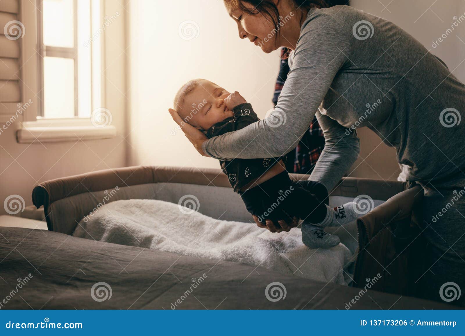 Mother Putting Her Baby To Sleep On A Bedside Baby Crib Stock Photo