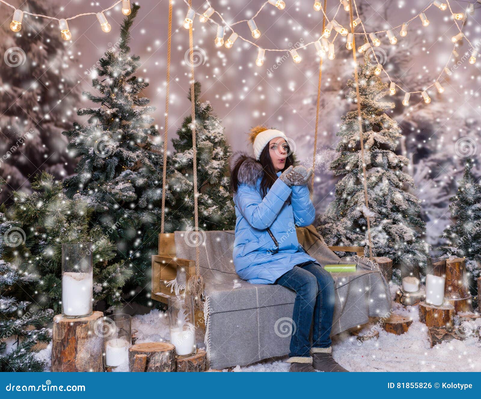 Woman in Blue Down Jacket Blows Snowflakes while Sitting on a Sw Stock ...