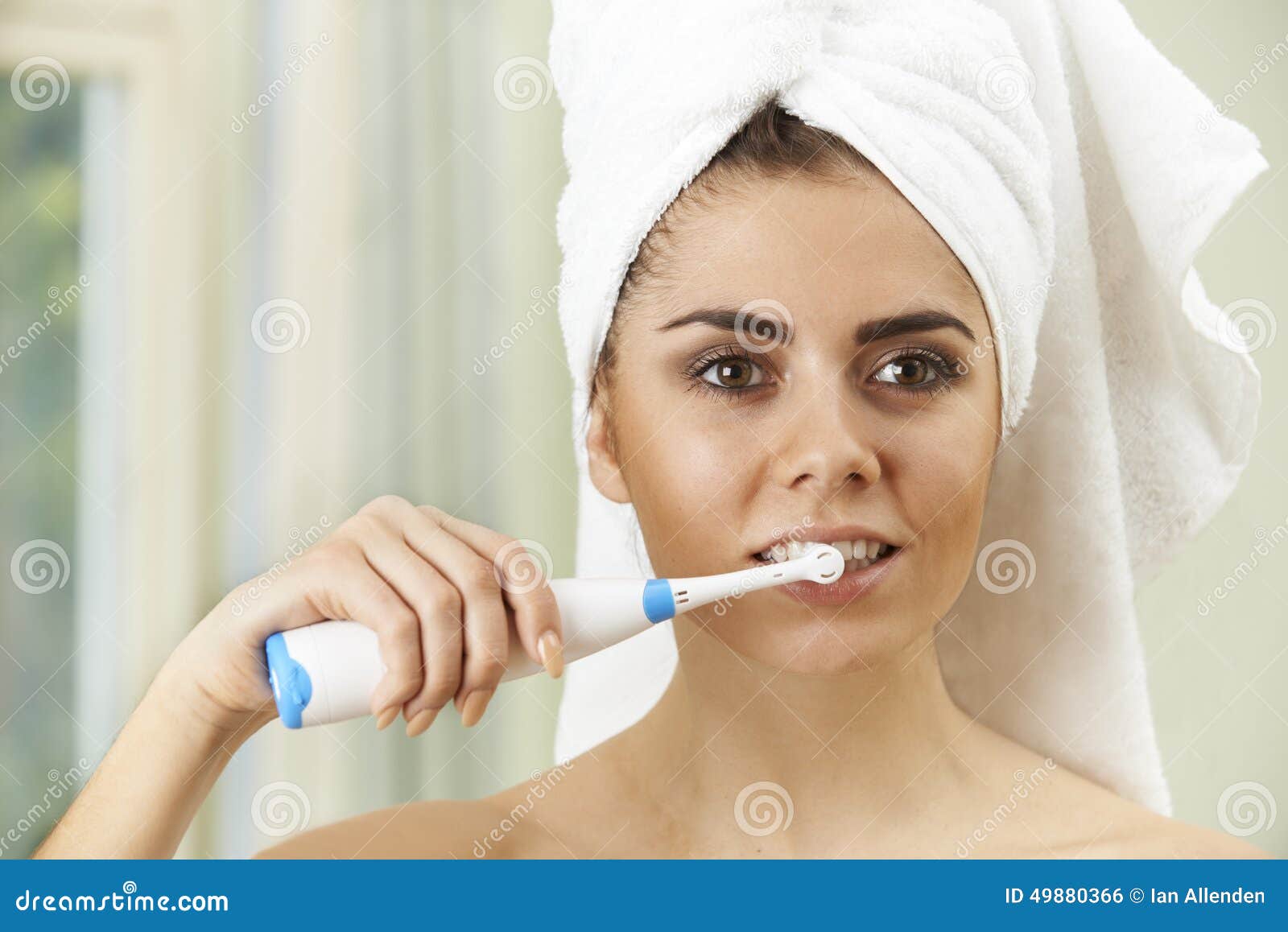 Woman Brushing Teeth with Electric Toothbrush in Bathroom Stock Photo