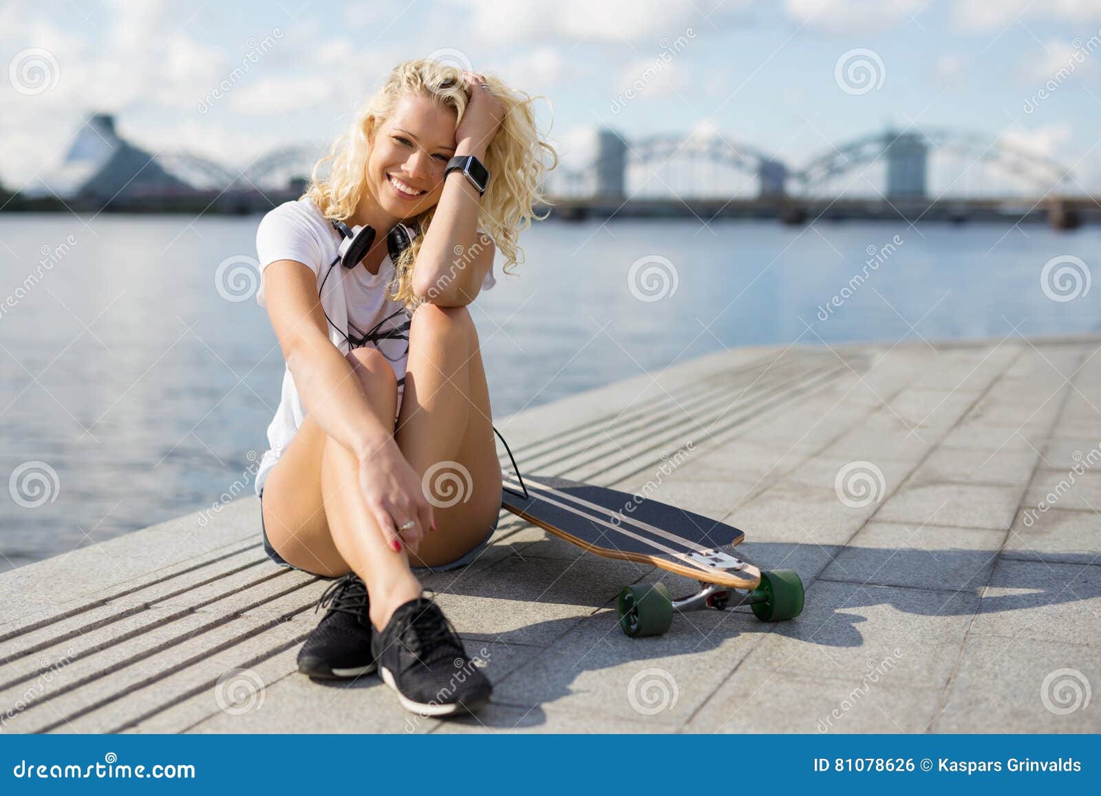woman in city sitting on pavement with longboard