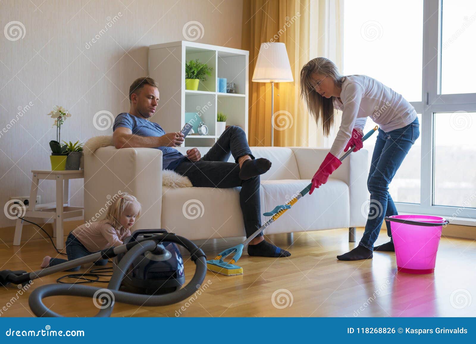 woman cleaning floors at home while her lazy man sitting in couch