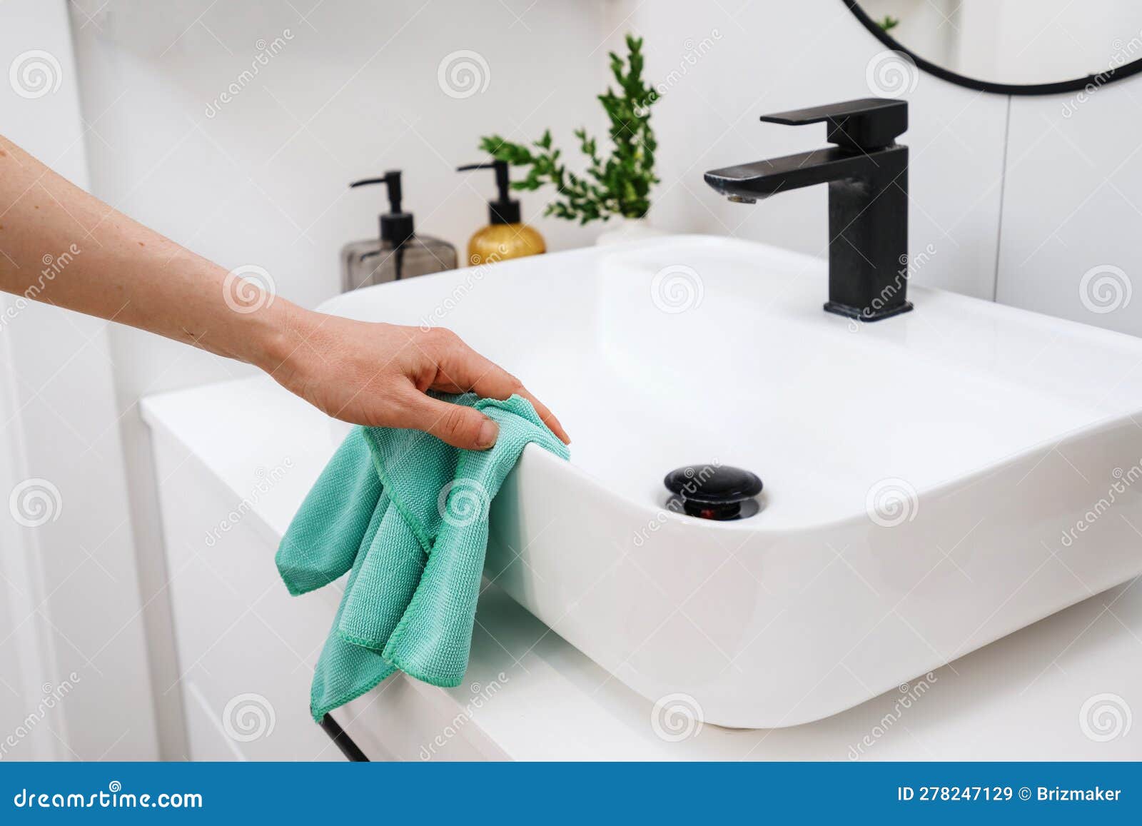 woman cleaning white washbowl with a black tap in bathroom