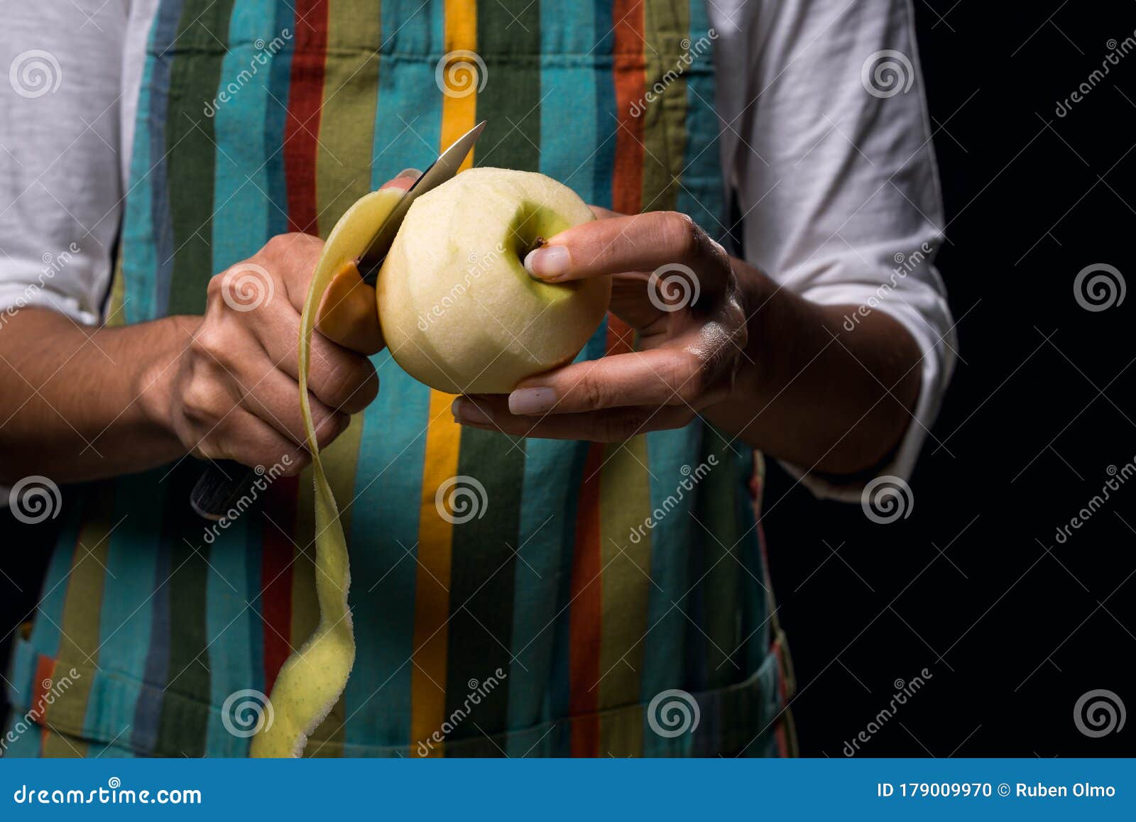 woman in colored apron peeling apple. dark black background