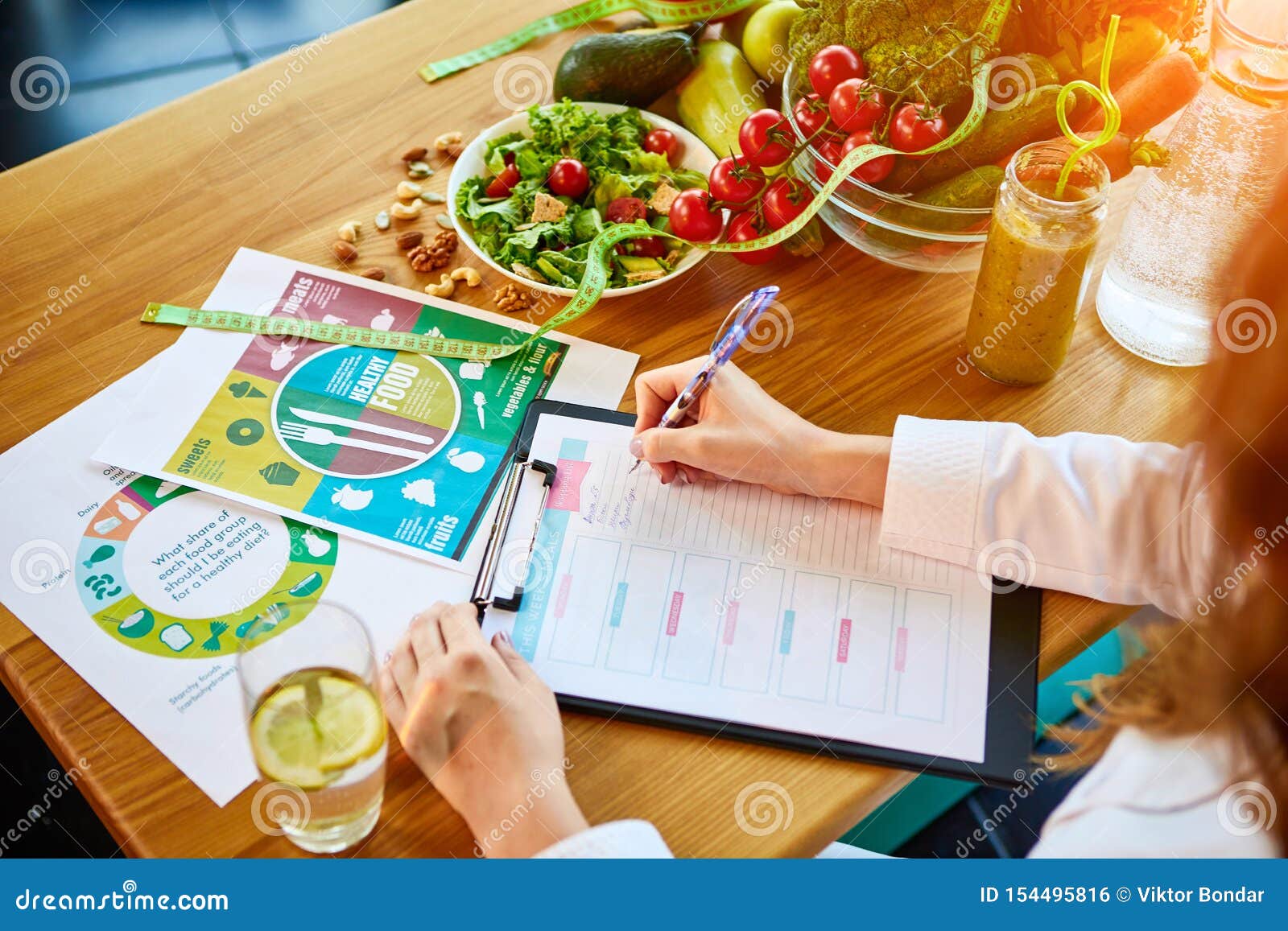 woman dietitian in medical uniform with tape measure working on a diet plan sitting with different healthy food ingredients in the