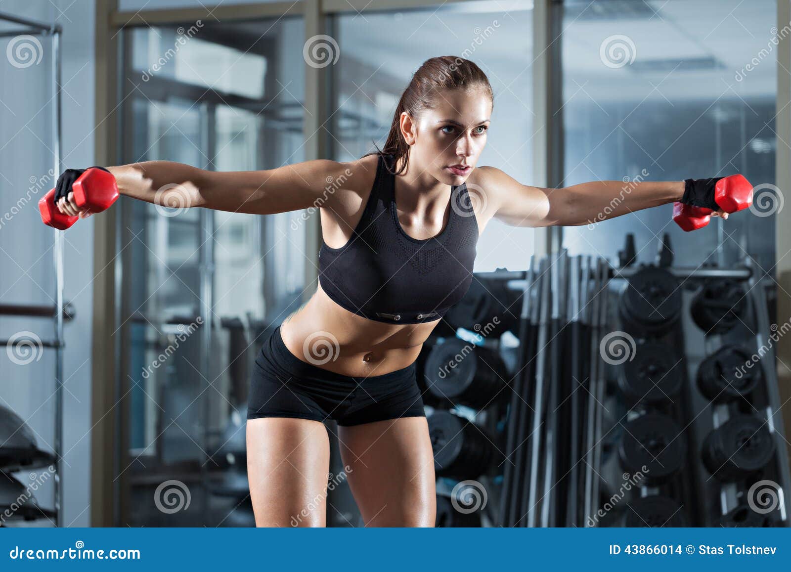 Woman doing workout with barbell. Sportive young woman doing exercise with barbell in the gym