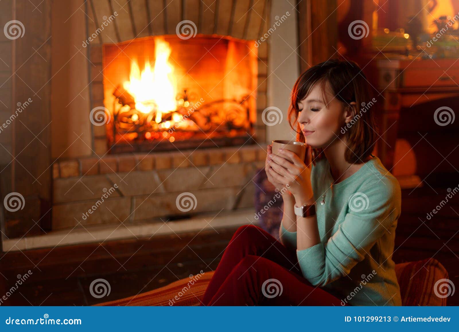 woman is drinking tea and warming herself by the fireplace. young caucasian female holds cup of coffee at home. warm