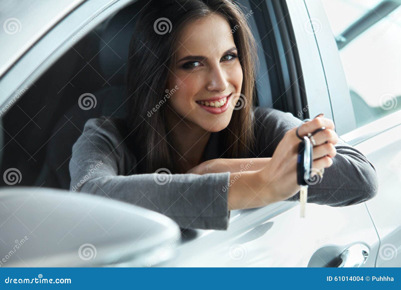 woman driver holding car keys siting in her new car.