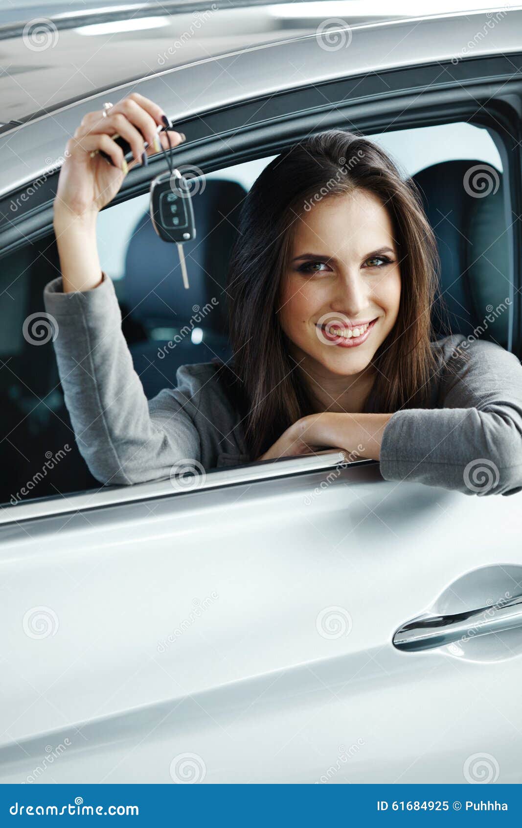 woman driver holding car keys siting in her new car.