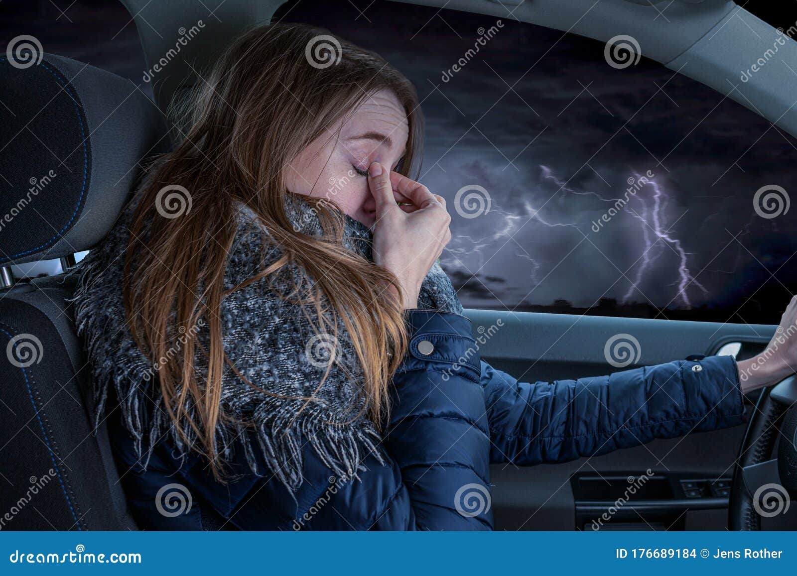 woman driving overtired car during thunderstorm and rubbing her eyes