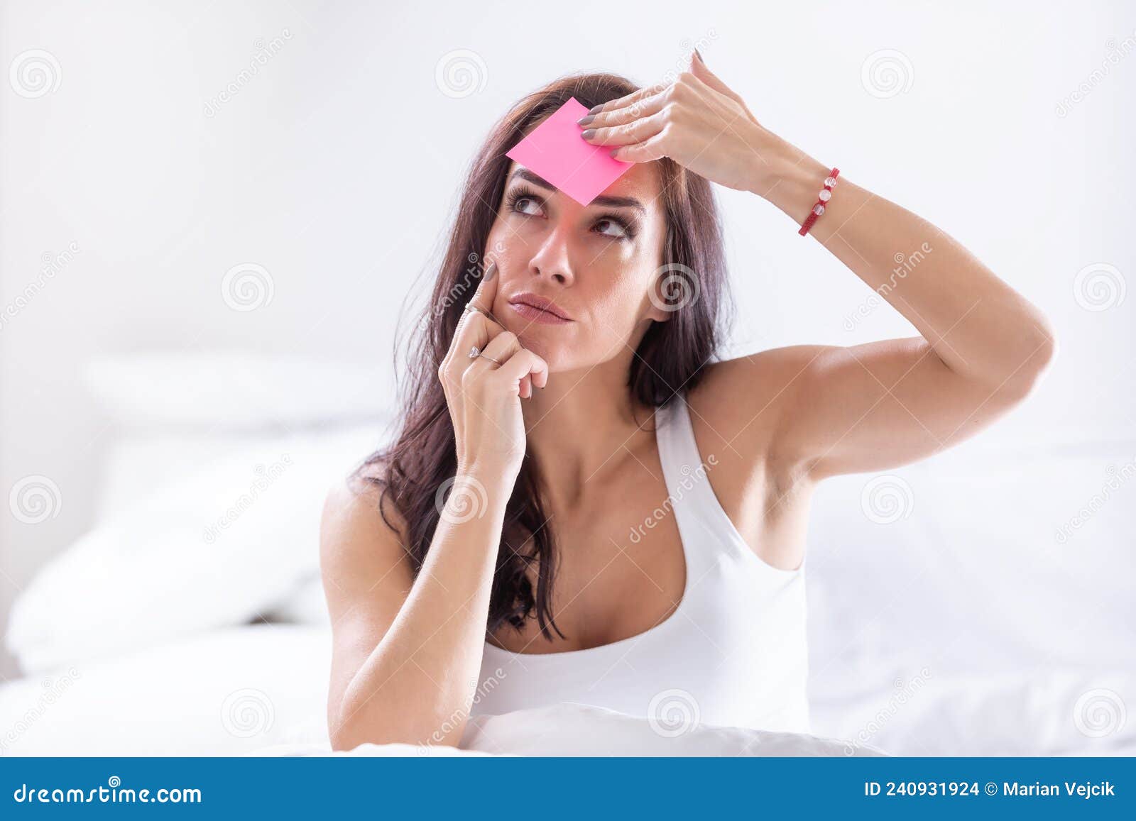 woman forgetting something puts a pink post-it on her forehead, thinking
