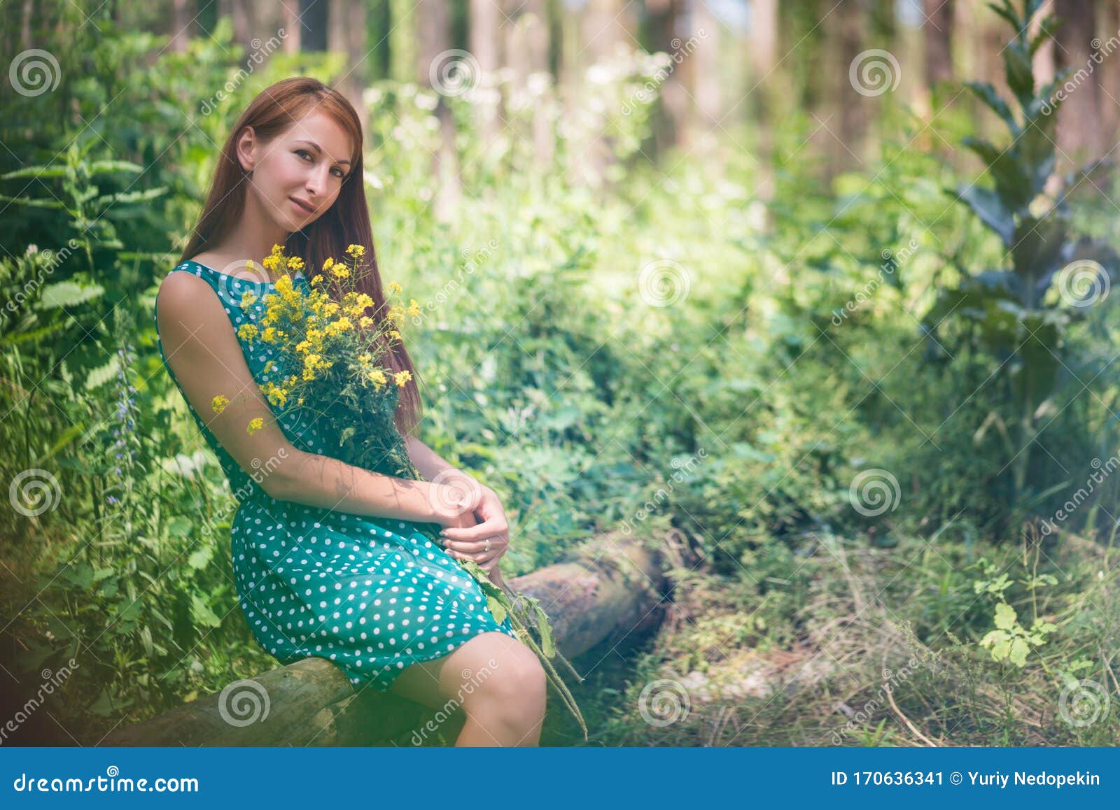 Woman in Green Dress Sitting on Log and Holding Yellow Flowers in ...