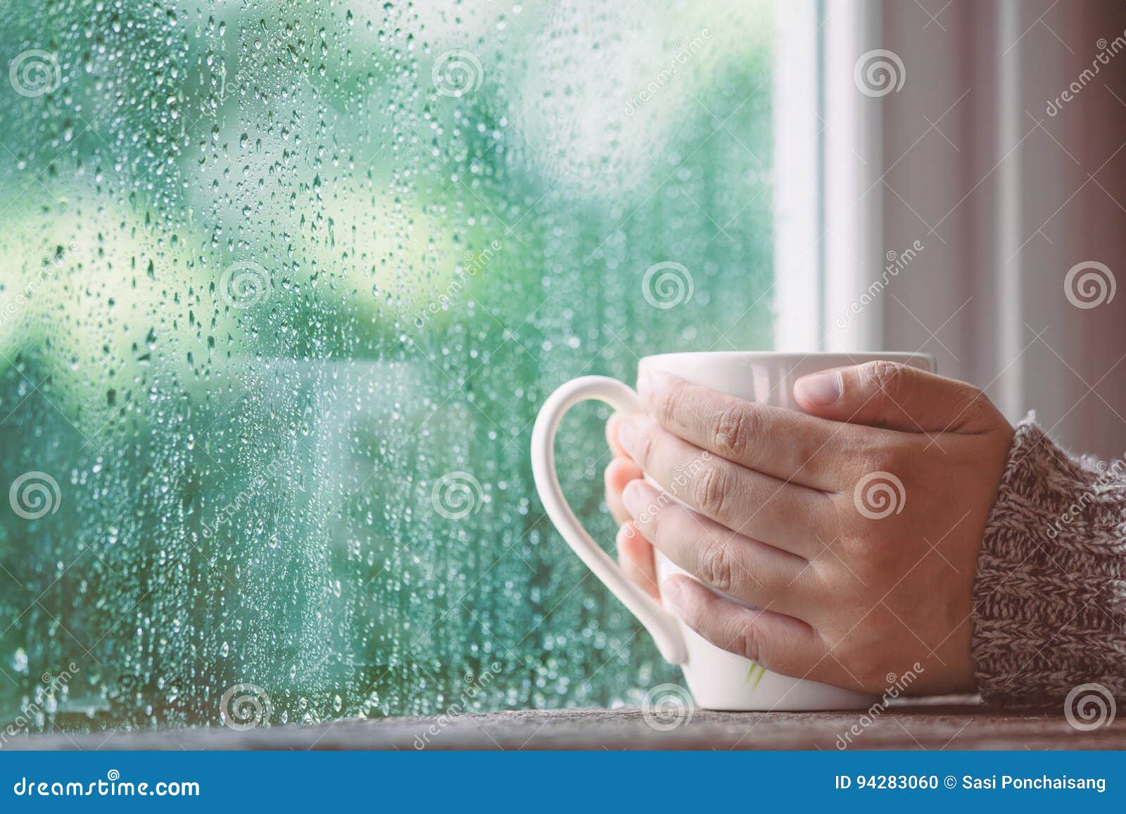 woman hand holding the cup of coffee or tea on rainy day window